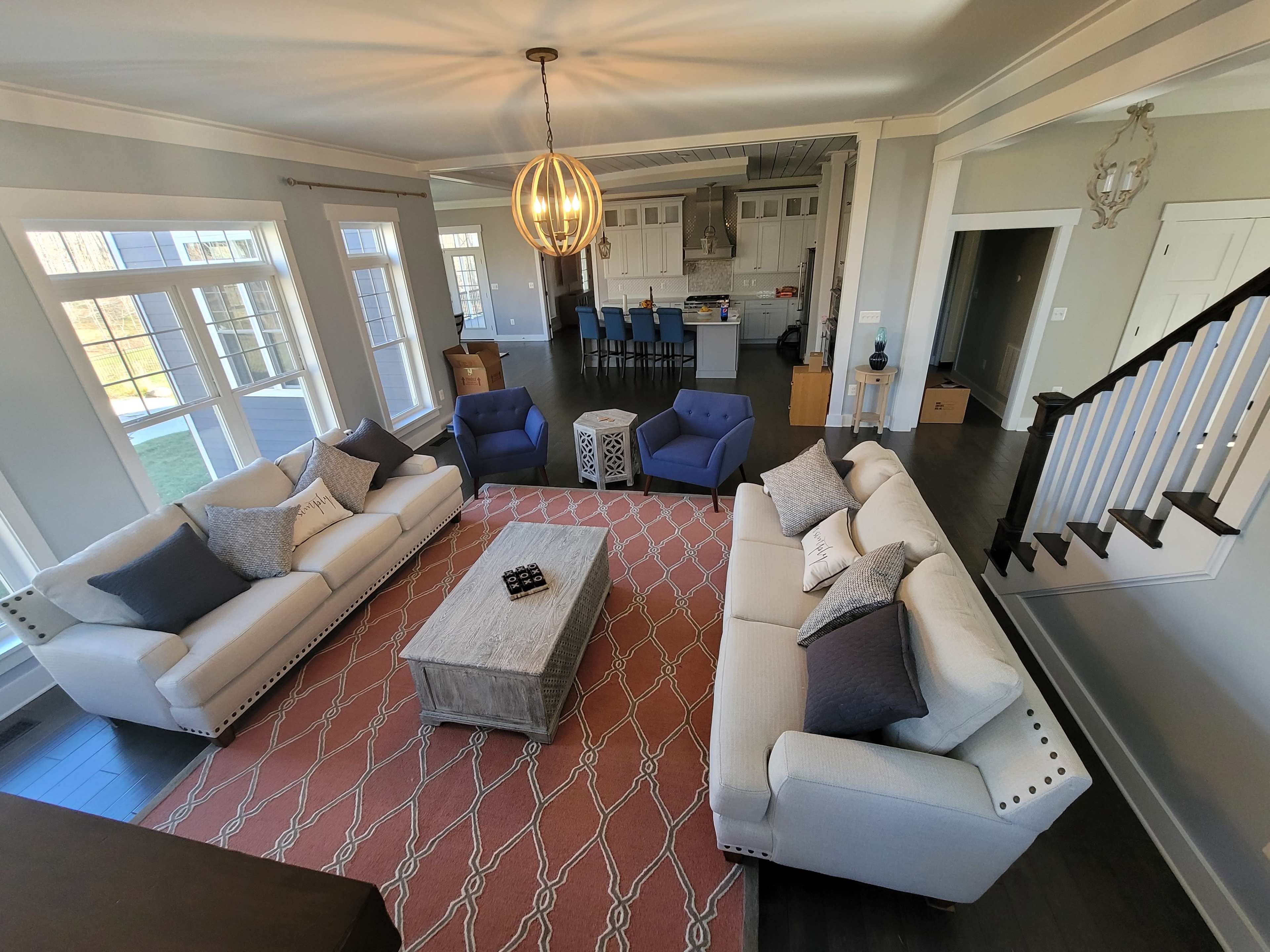 A spacious living area with two sofas, two blue armchairs, a center coffee table, and a patterned rug, leading into an open kitchen.