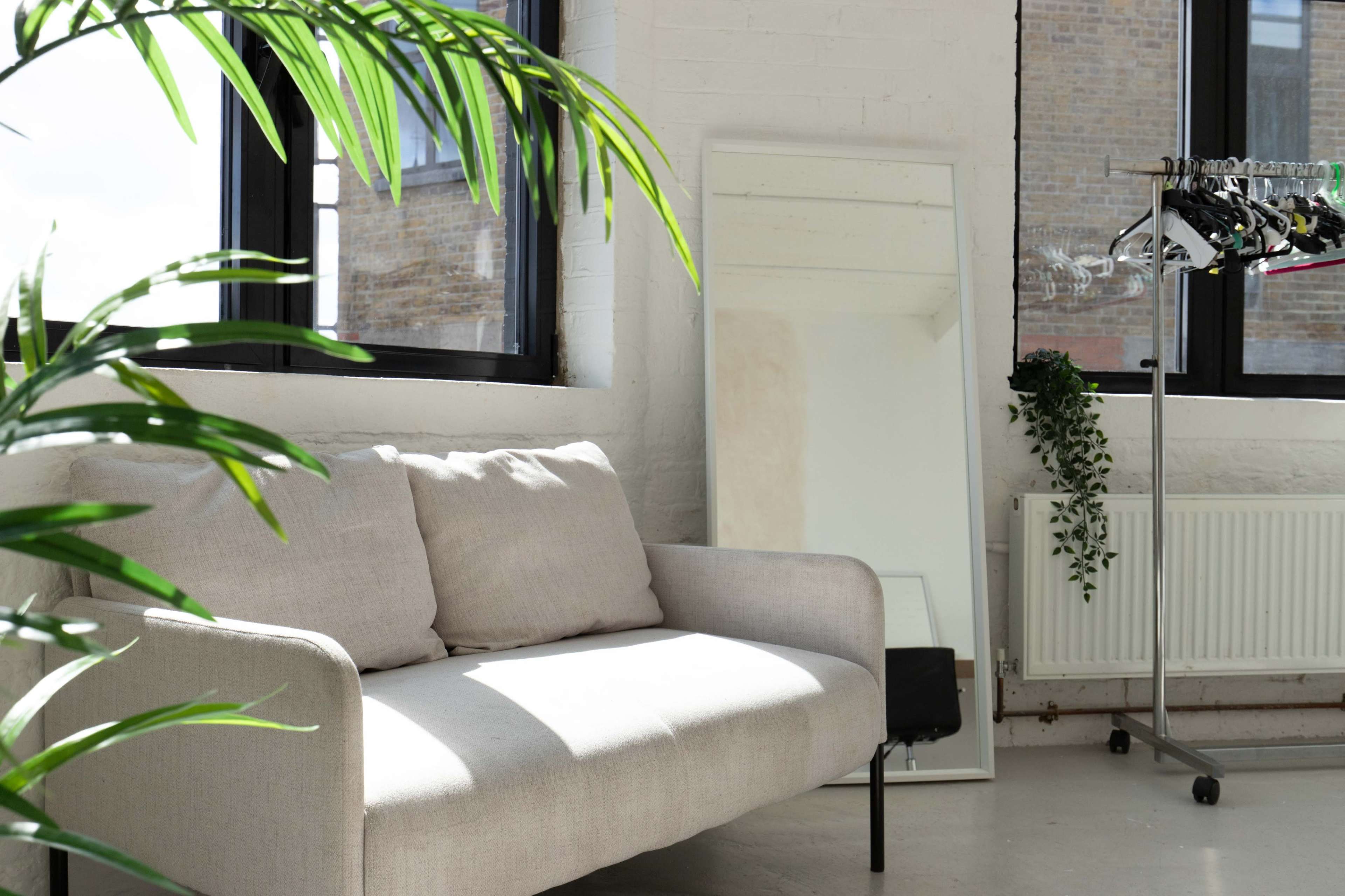 A light-filled room features a beige sofa, a tall mirror, and a clothing rack with hangers.