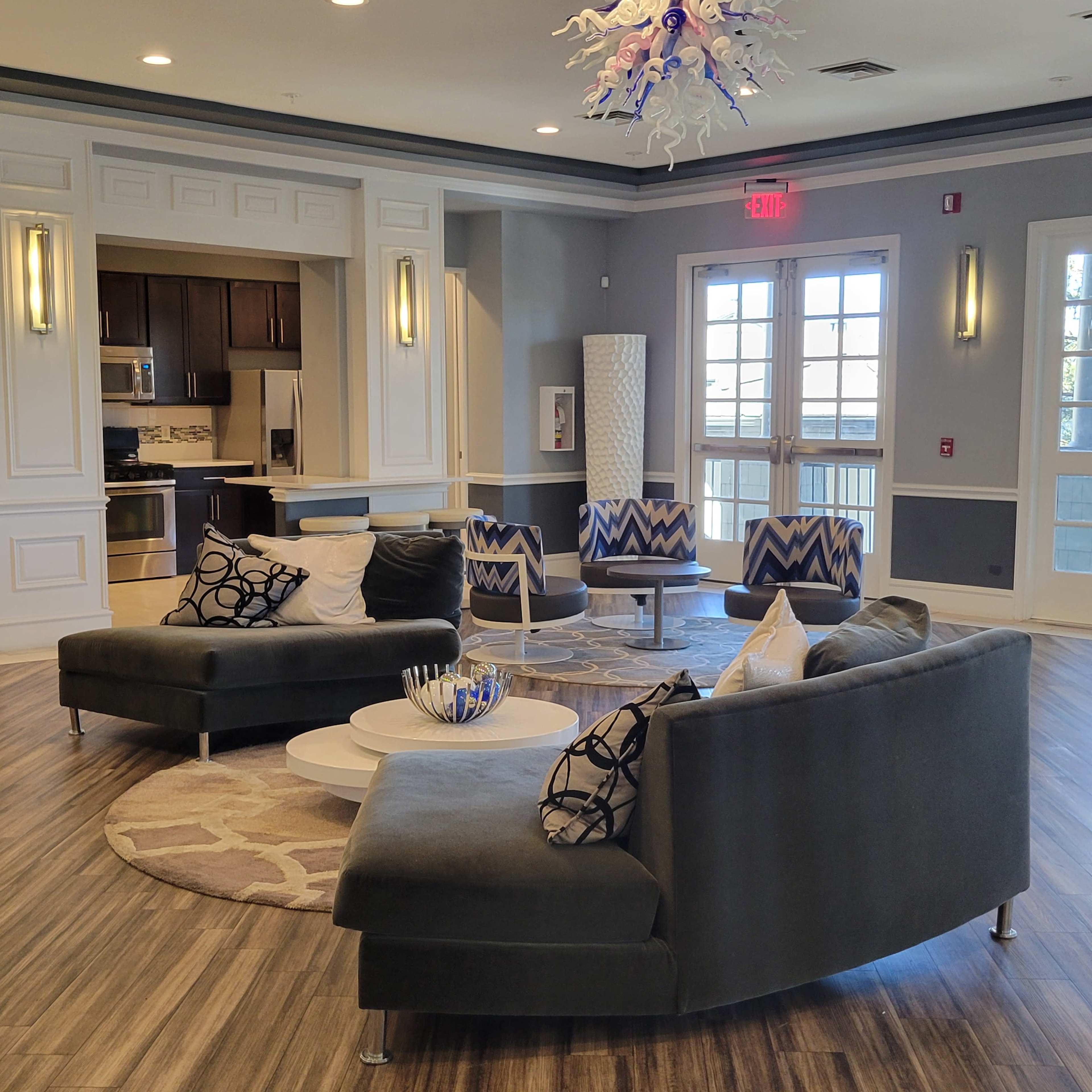 A modern lounge area featuring curved sofas, patterned chairs, a coffee table, and large windows letting in natural light.