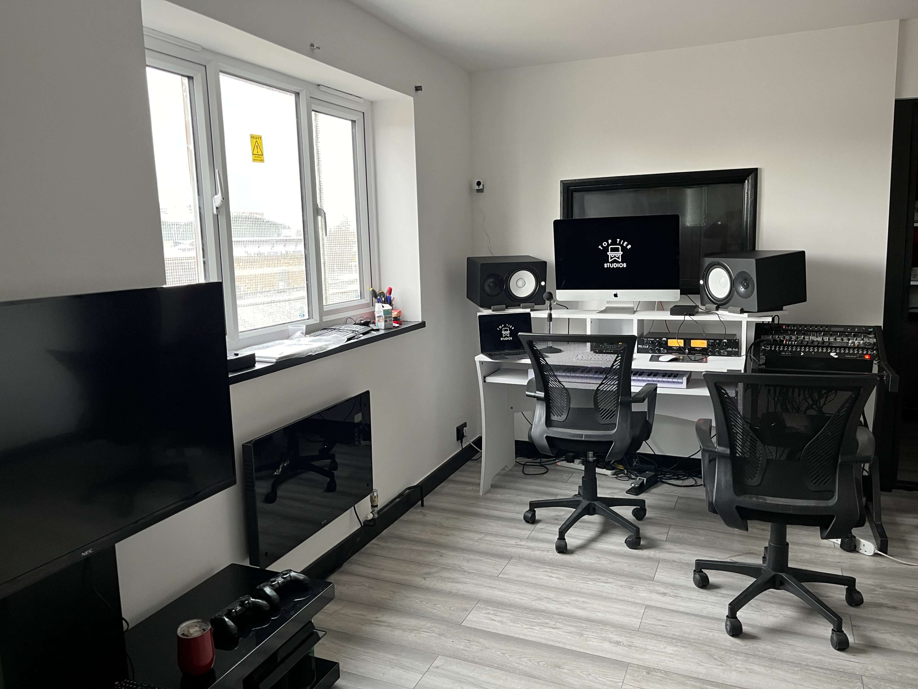 A modern music production studio with two desk chairs, a large desk with audio equipment, and a television in the corner.