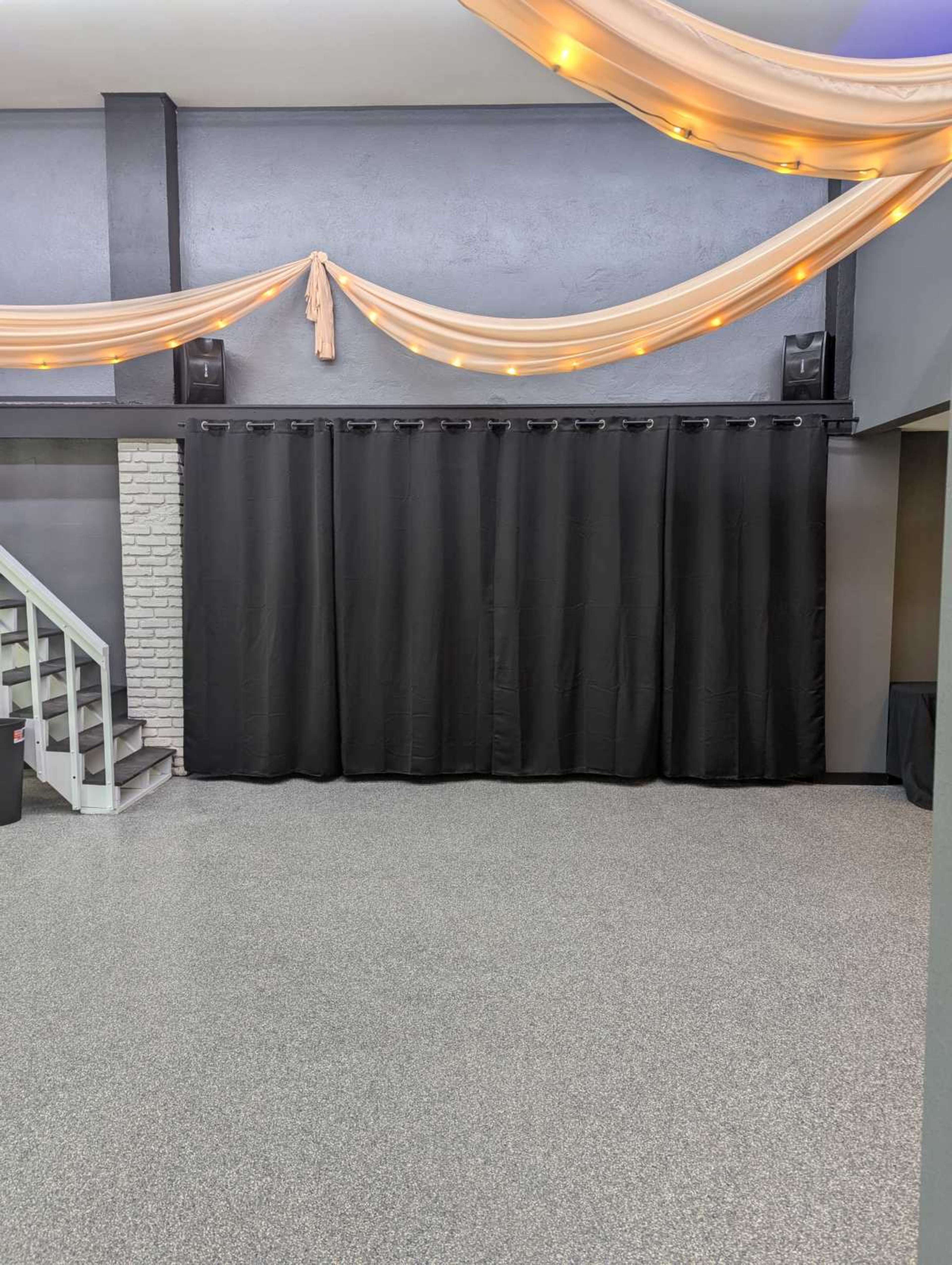 The image shows a spacious room with a polished floor, black curtains covering a wall, and decorative draping above with soft lighting.
