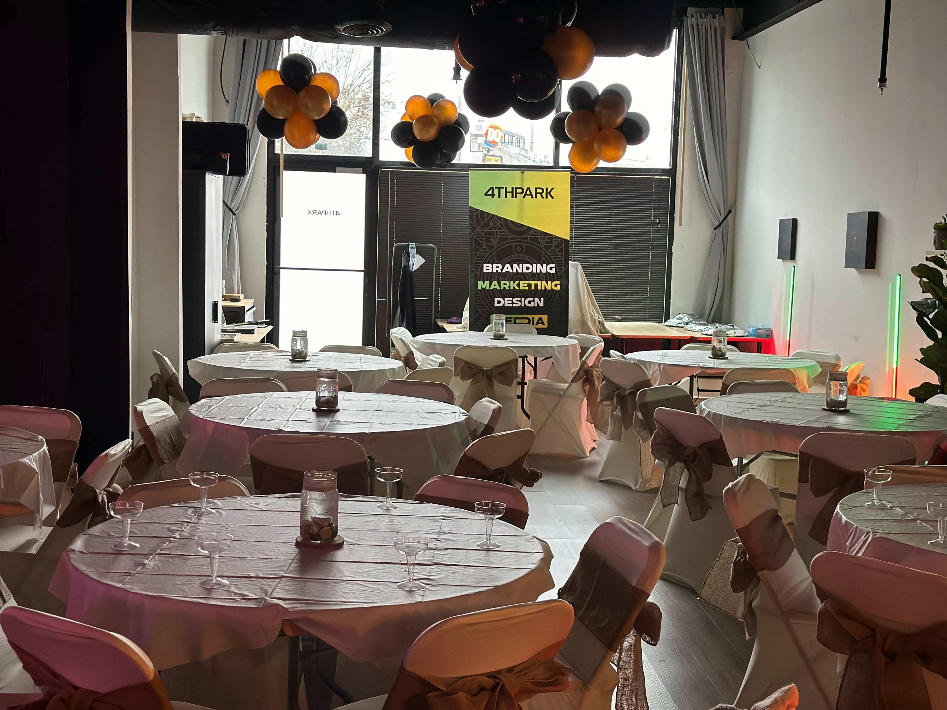 A decorated event space featuring round tables with white tablecloths and brown bows, along with a backdrop displaying branding information.