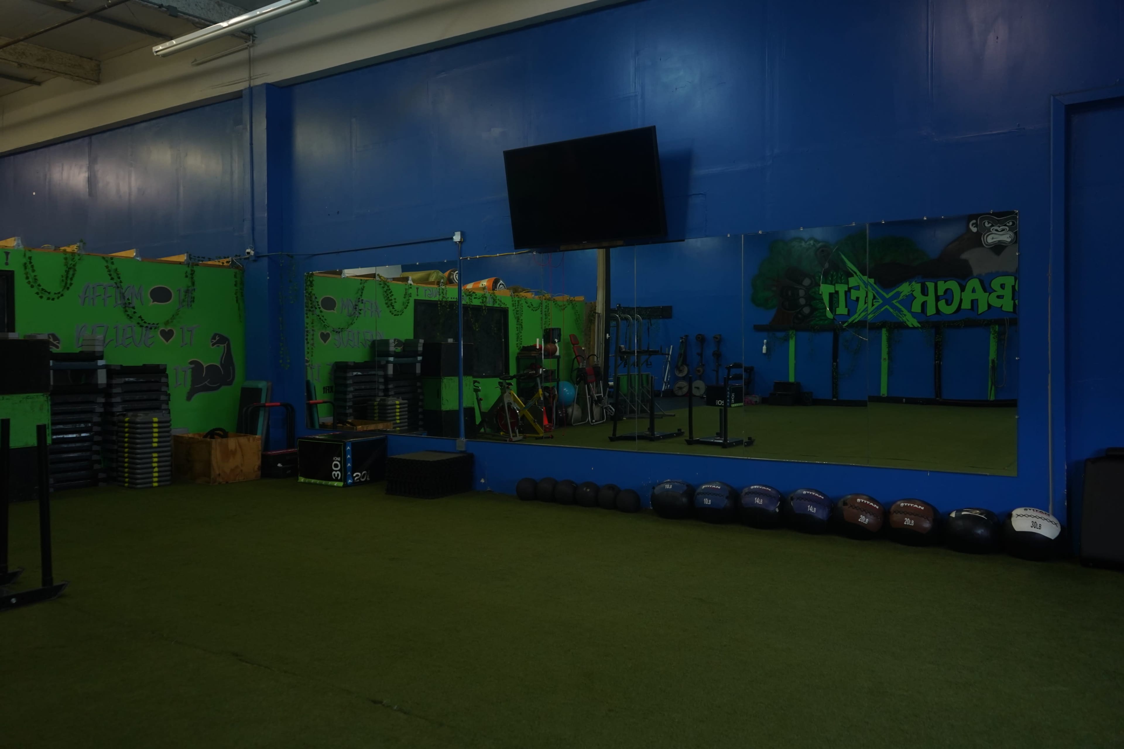 A gym interior features a large mirror, exercise equipment, and a green and blue color scheme on the walls.