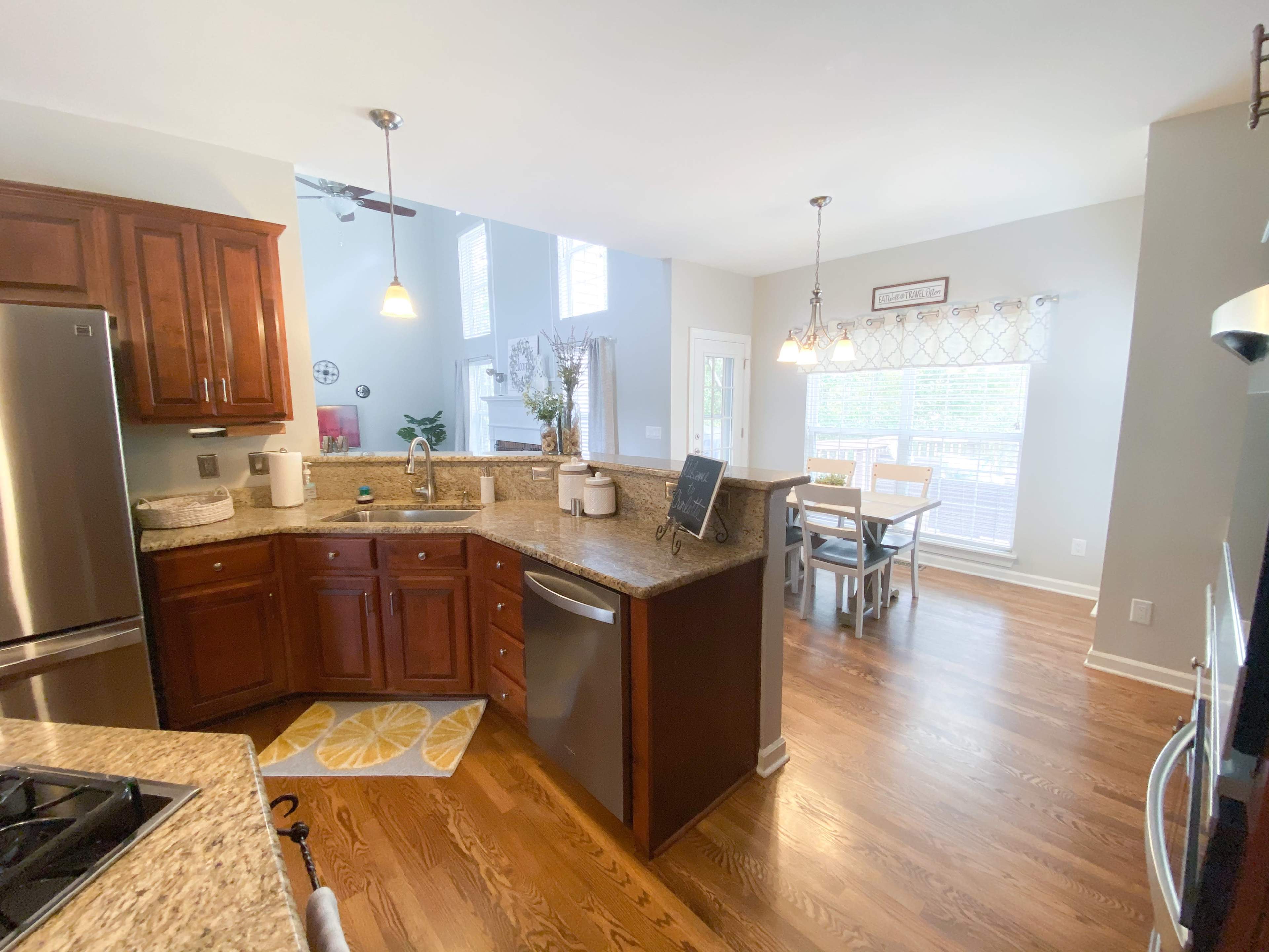 A modern kitchen features wooden cabinetry, granite countertops, and stainless steel appliances, connected to a dining area with a table and chairs.