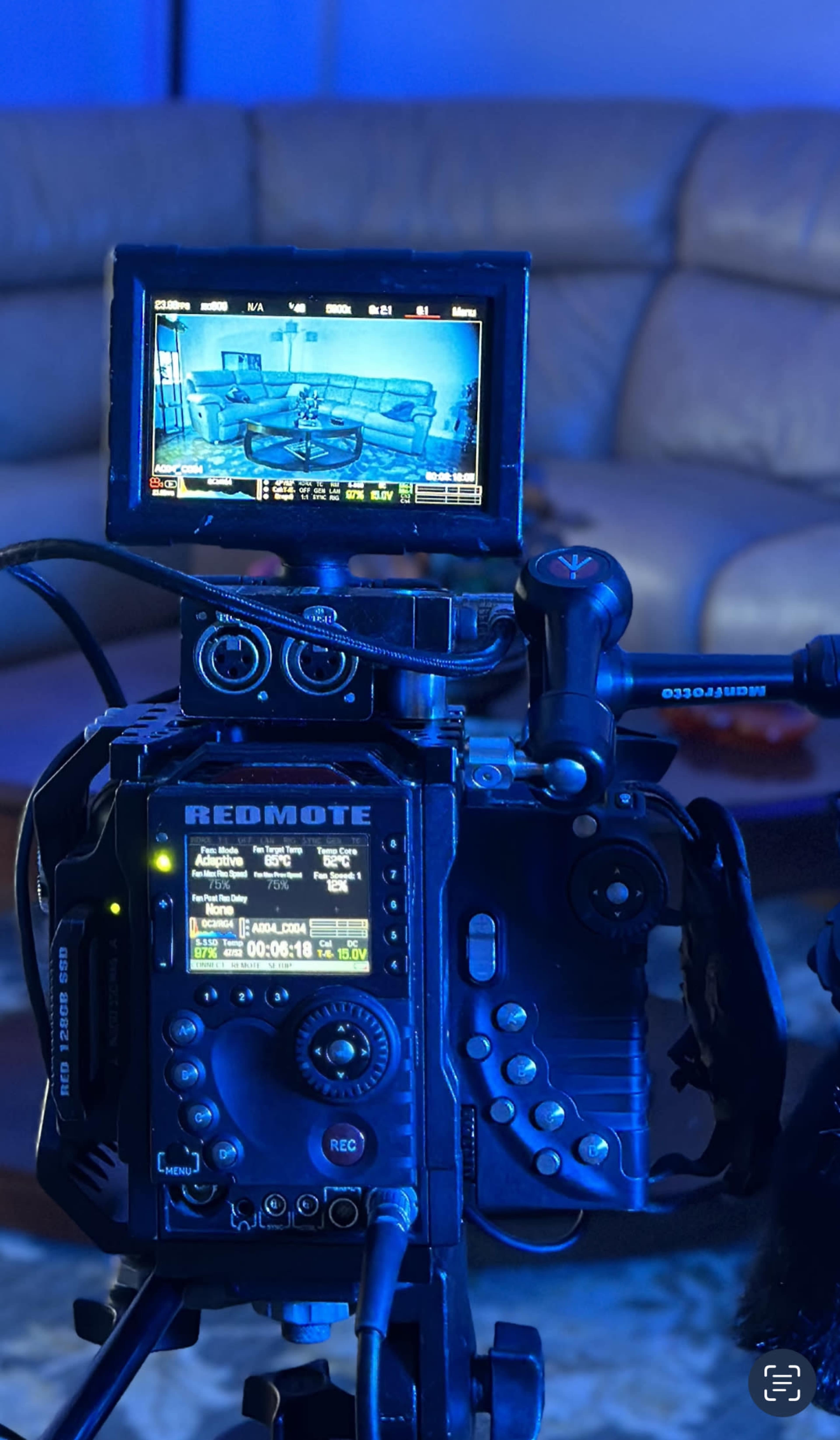 A professional camera setup displays a monitor showing a living room scene in blue lighting.