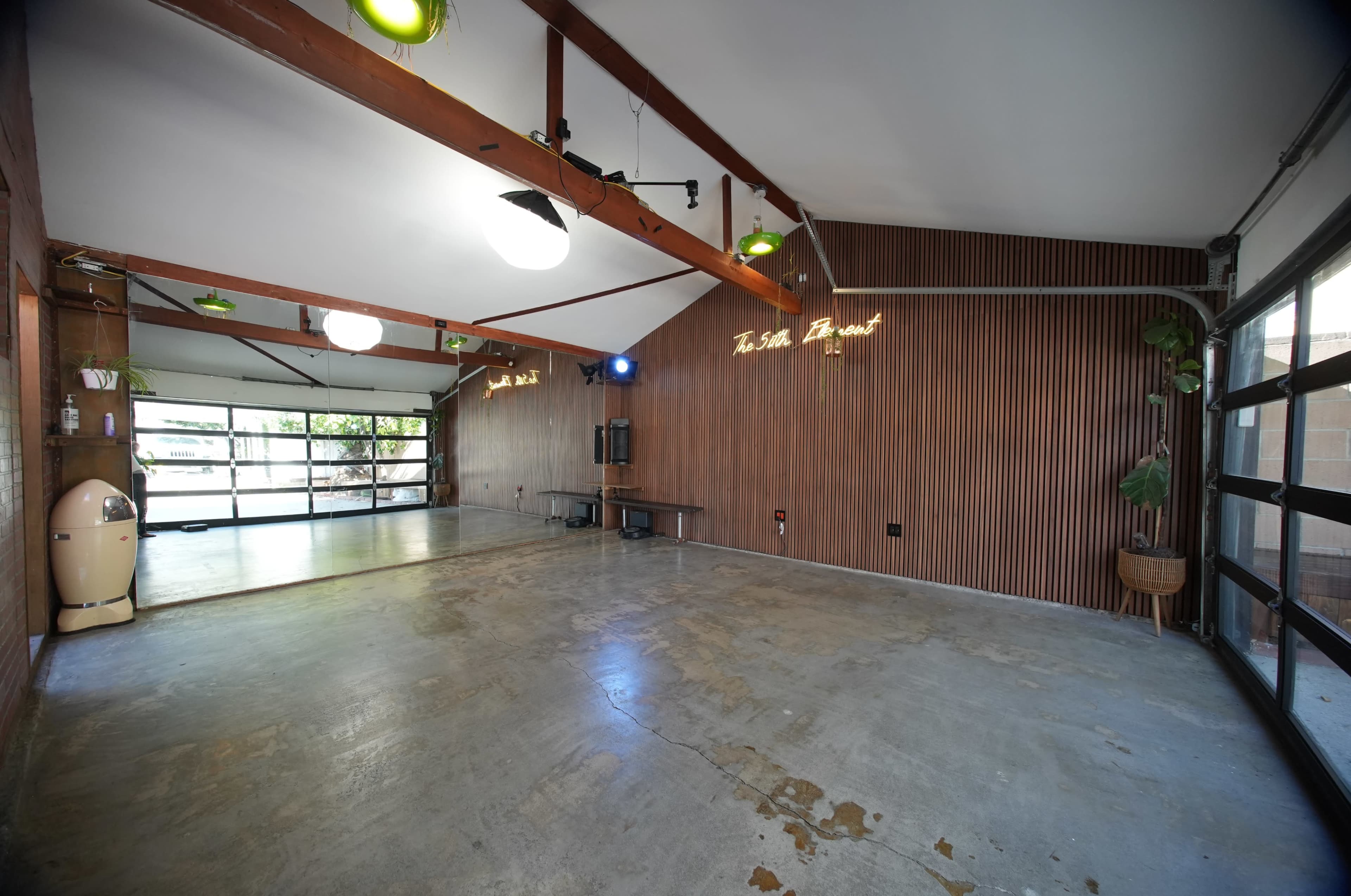 The image shows an empty room with wooden wall paneling, a concrete floor, and large glass doors that open to an outdoor area.