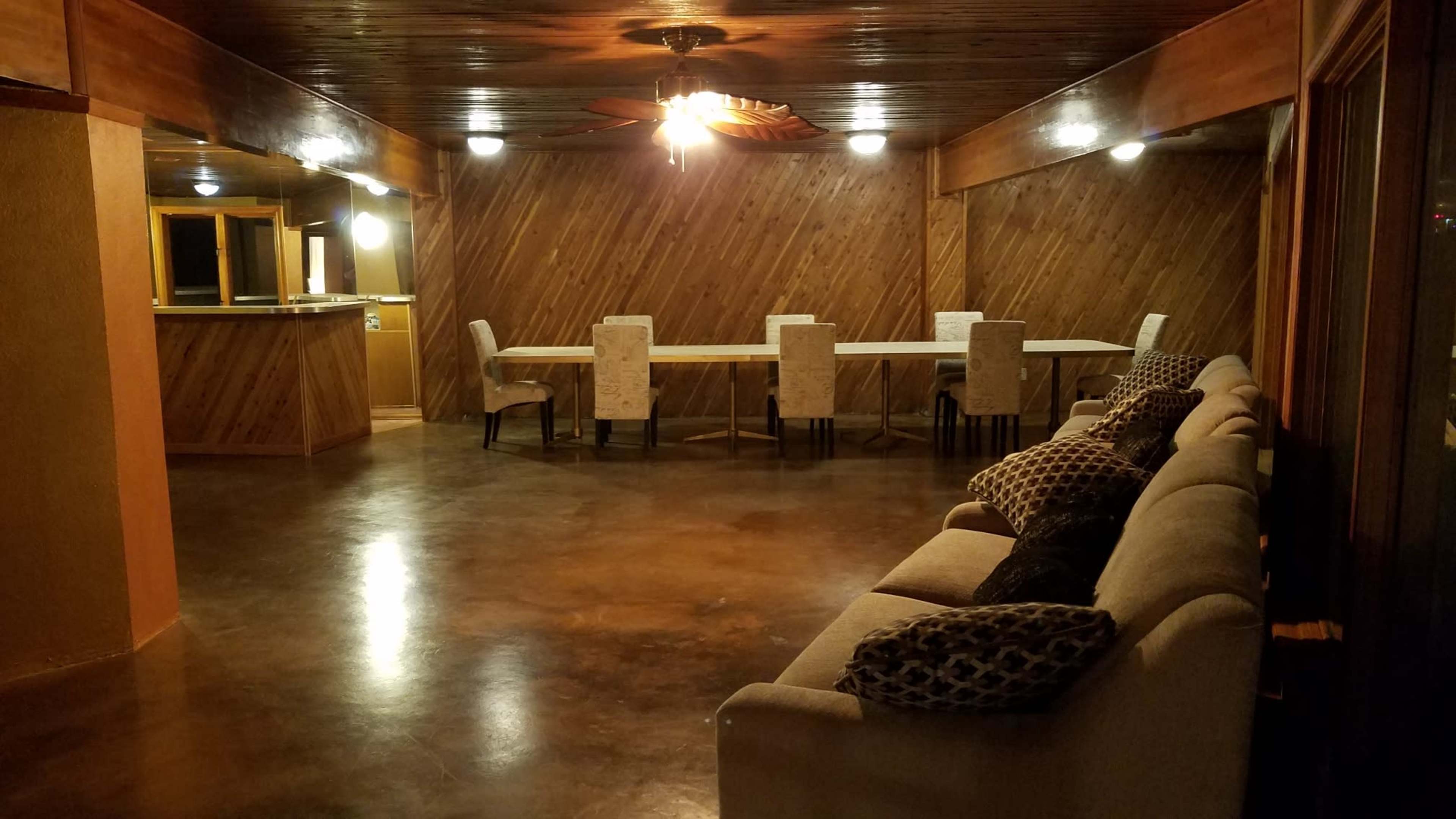 A spacious room features a long table with chairs, a couch along one wall, and wooden paneling on the walls and ceiling.
