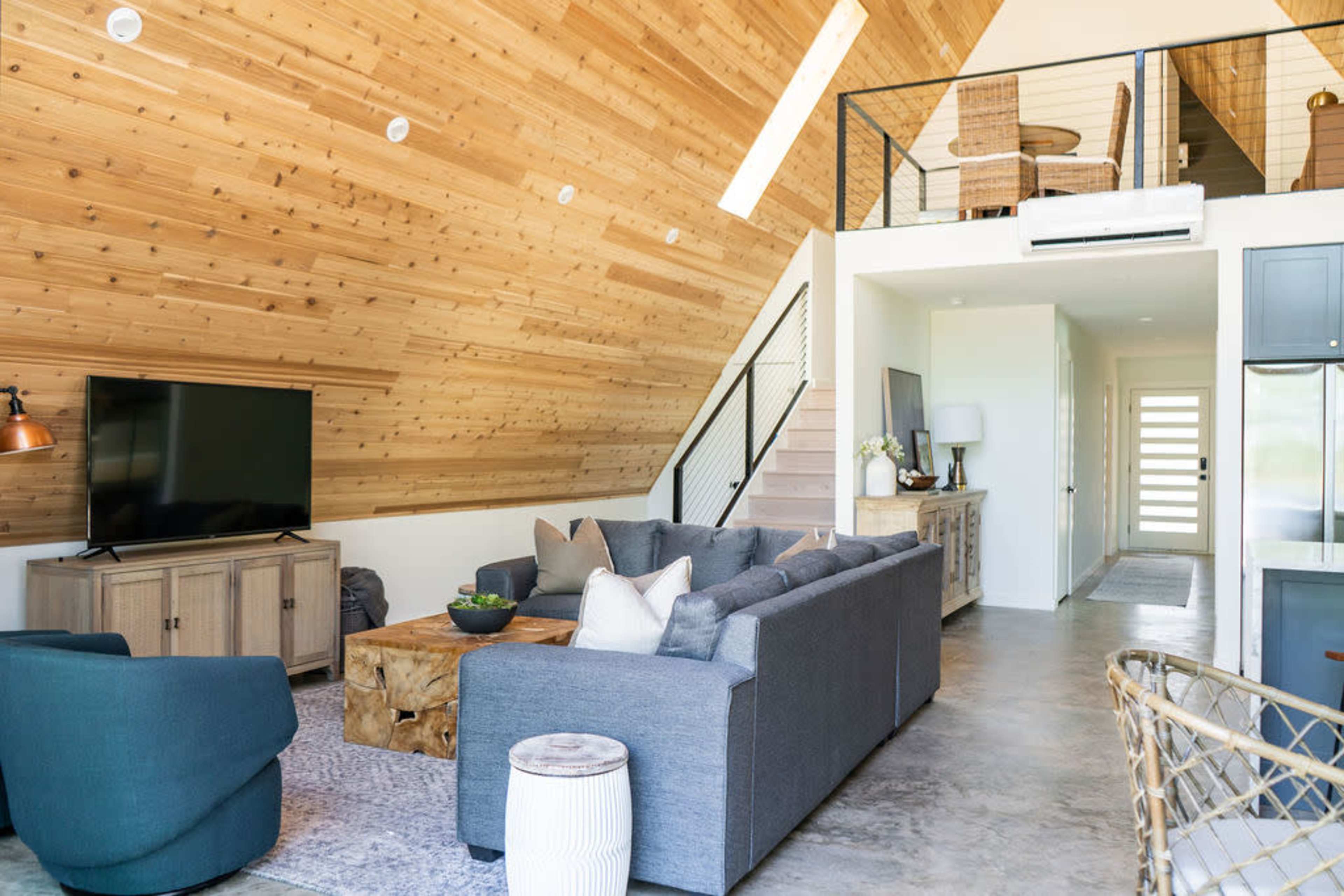 A modern living room with a high ceiling, wooden walls, a sectional sofa, and a television unit.