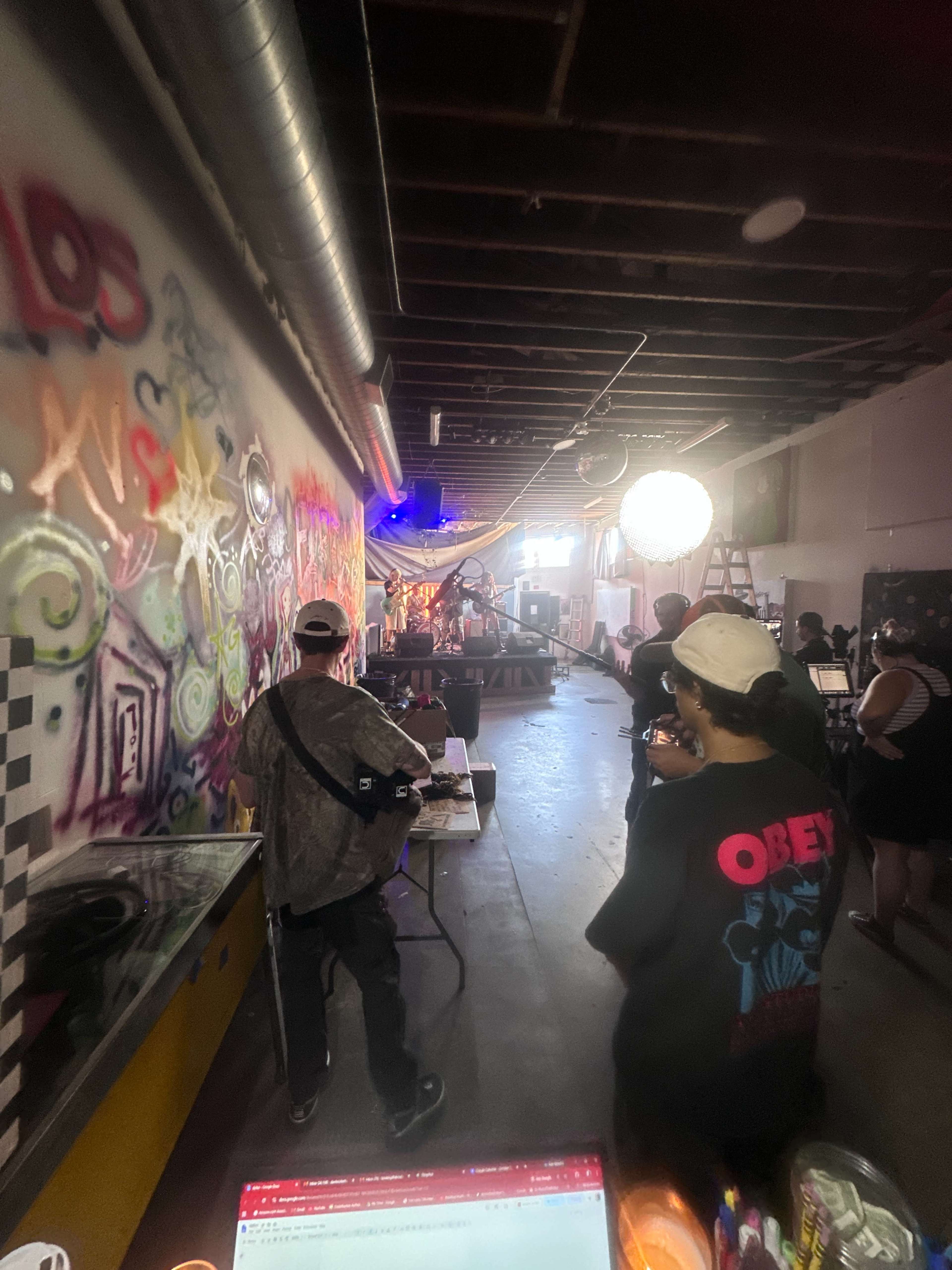 A band performs on a makeshift stage inside a graffiti-covered warehouse, while audience members watch from the darkened space.