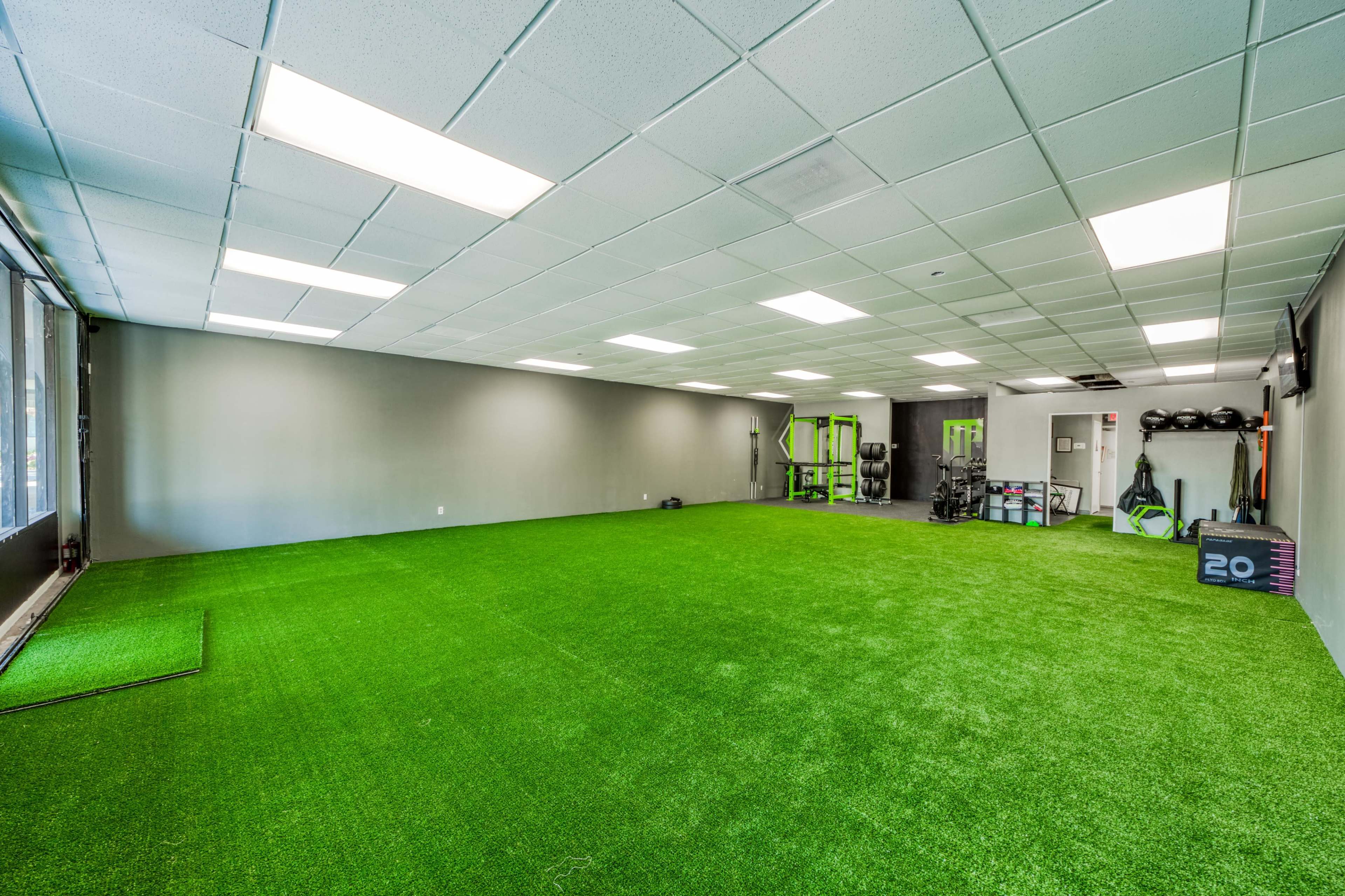 A spacious gym interior with artificial grass flooring, equipped with fitness equipment along the walls.