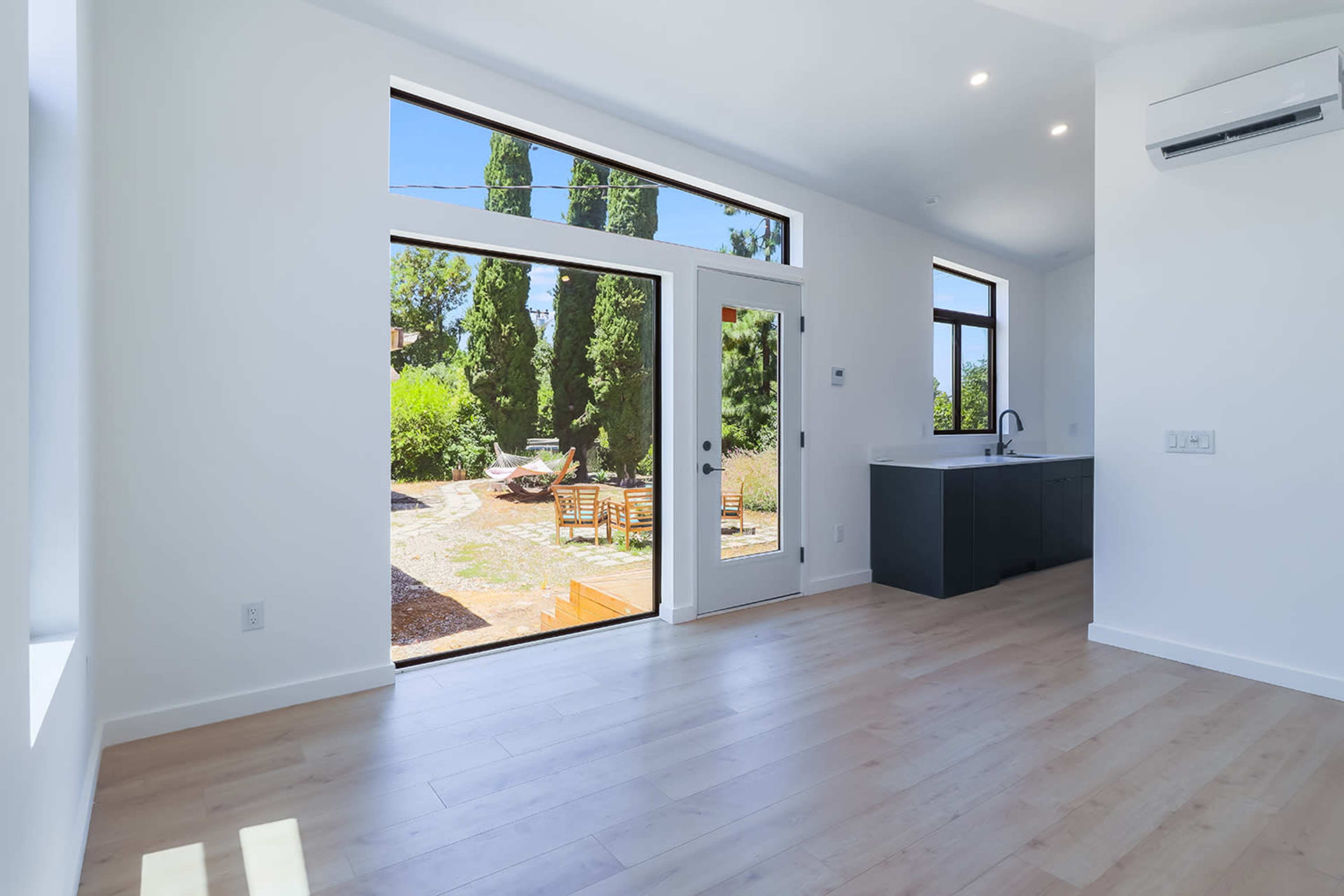 A bright, open interior space with large windows overlooking a landscaped garden and wooden outdoor seating area.