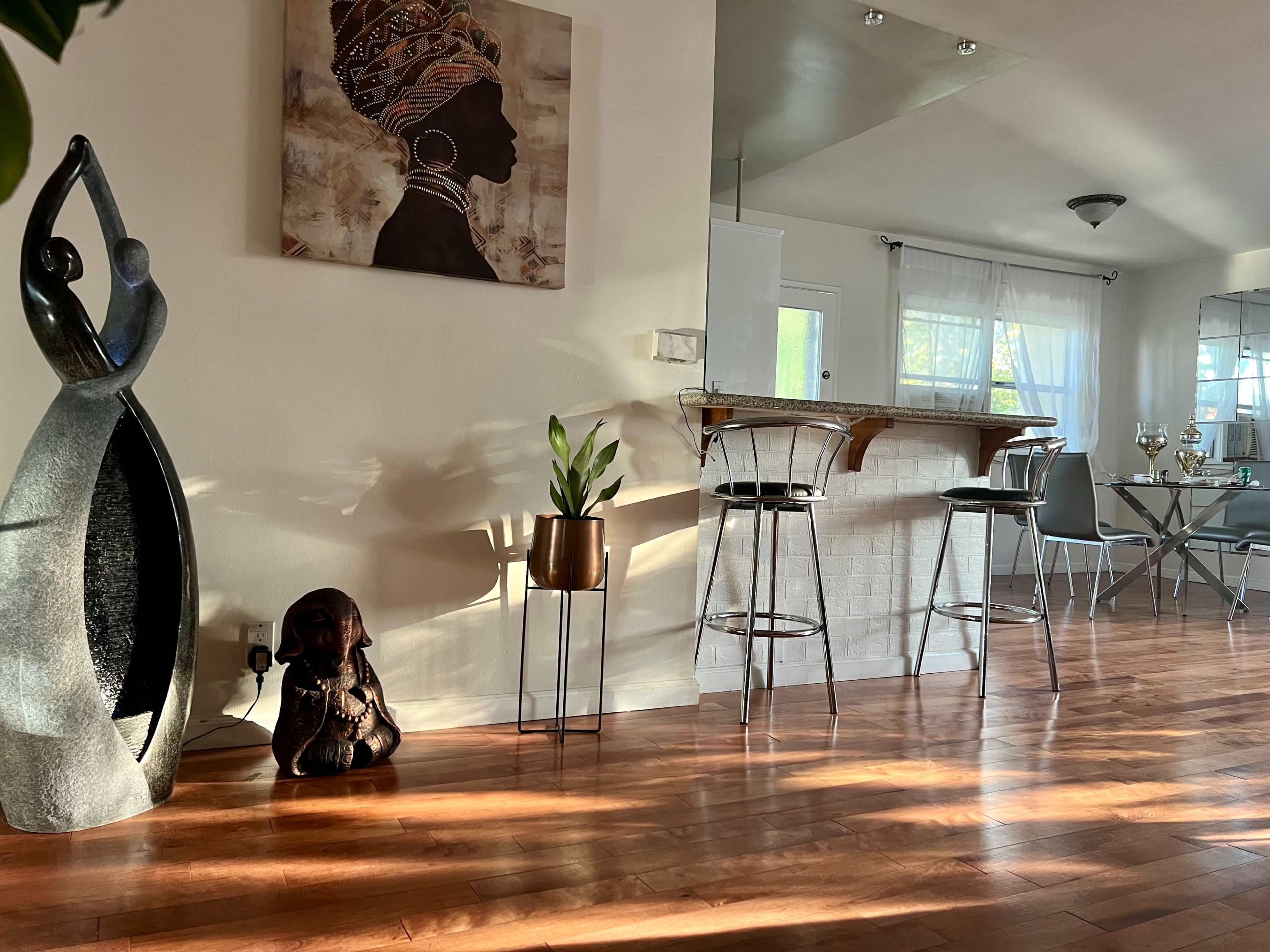 A modern living space featuring a bar area with stools, decorative sculptures, and a dining table.
