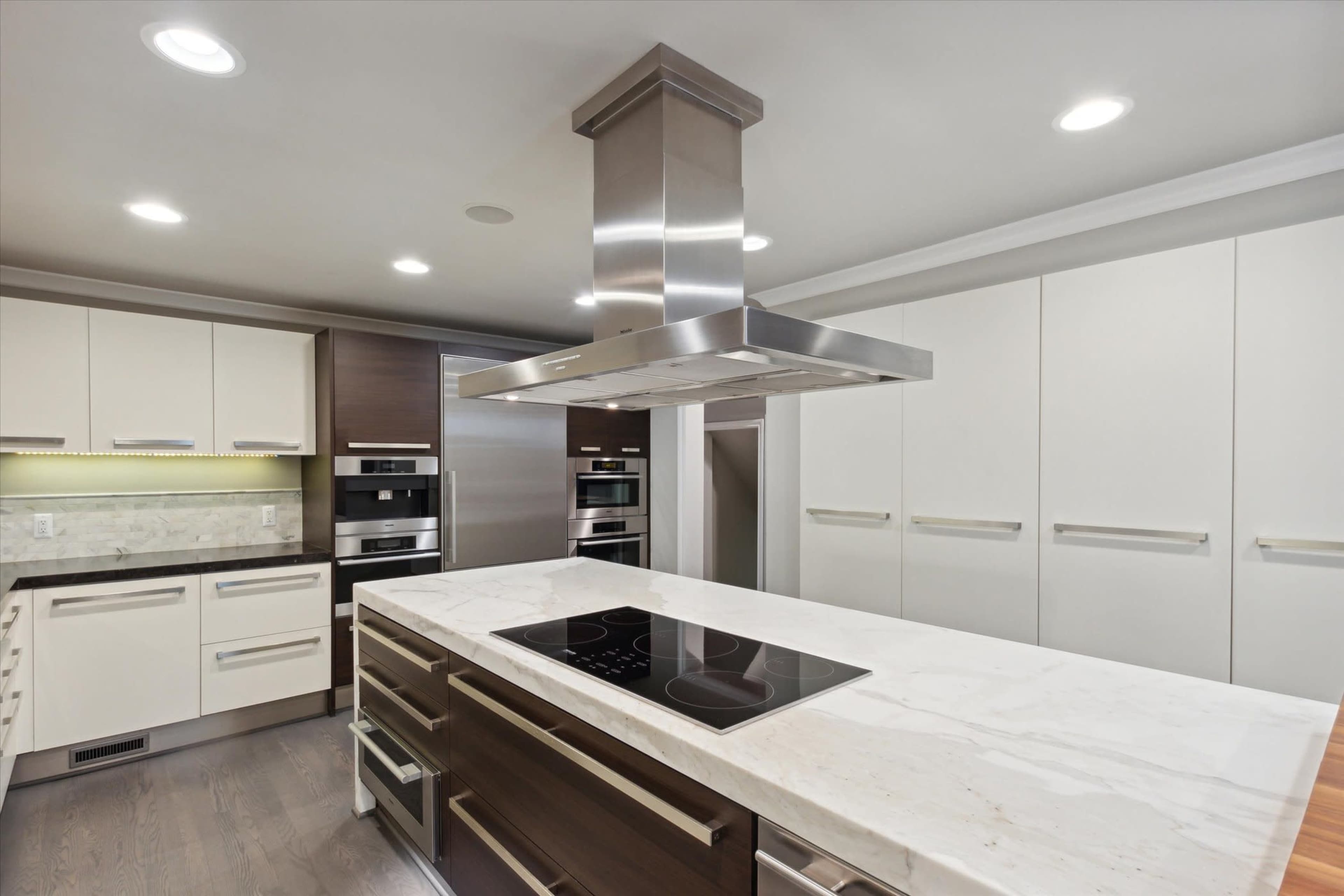 A modern kitchen featuring a central island with a cooktop, sleek cabinetry, and built-in ovens.