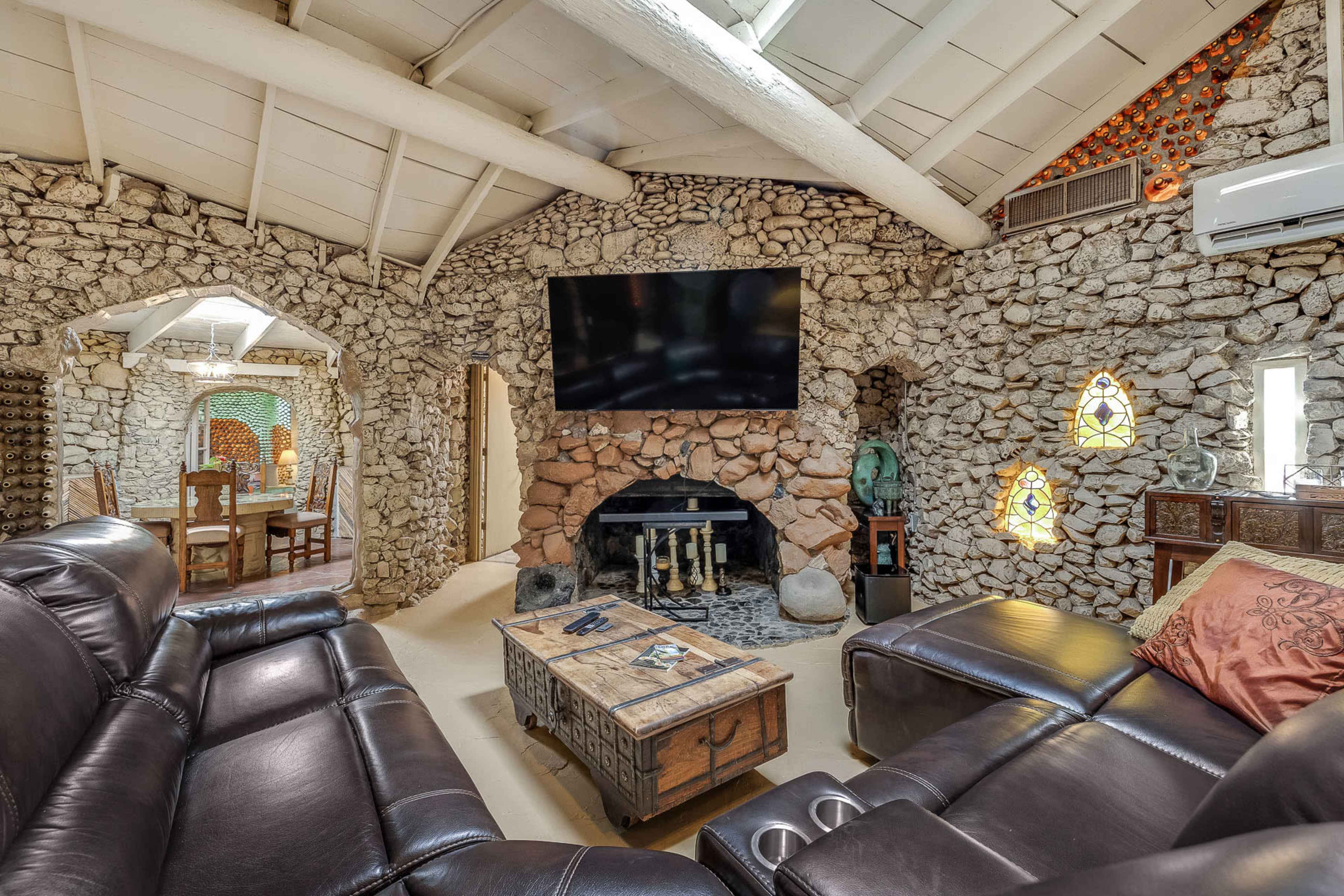 The interior features a stone wall design with a large television mounted above a fireplace, surrounded by leather seating and decorative elements.