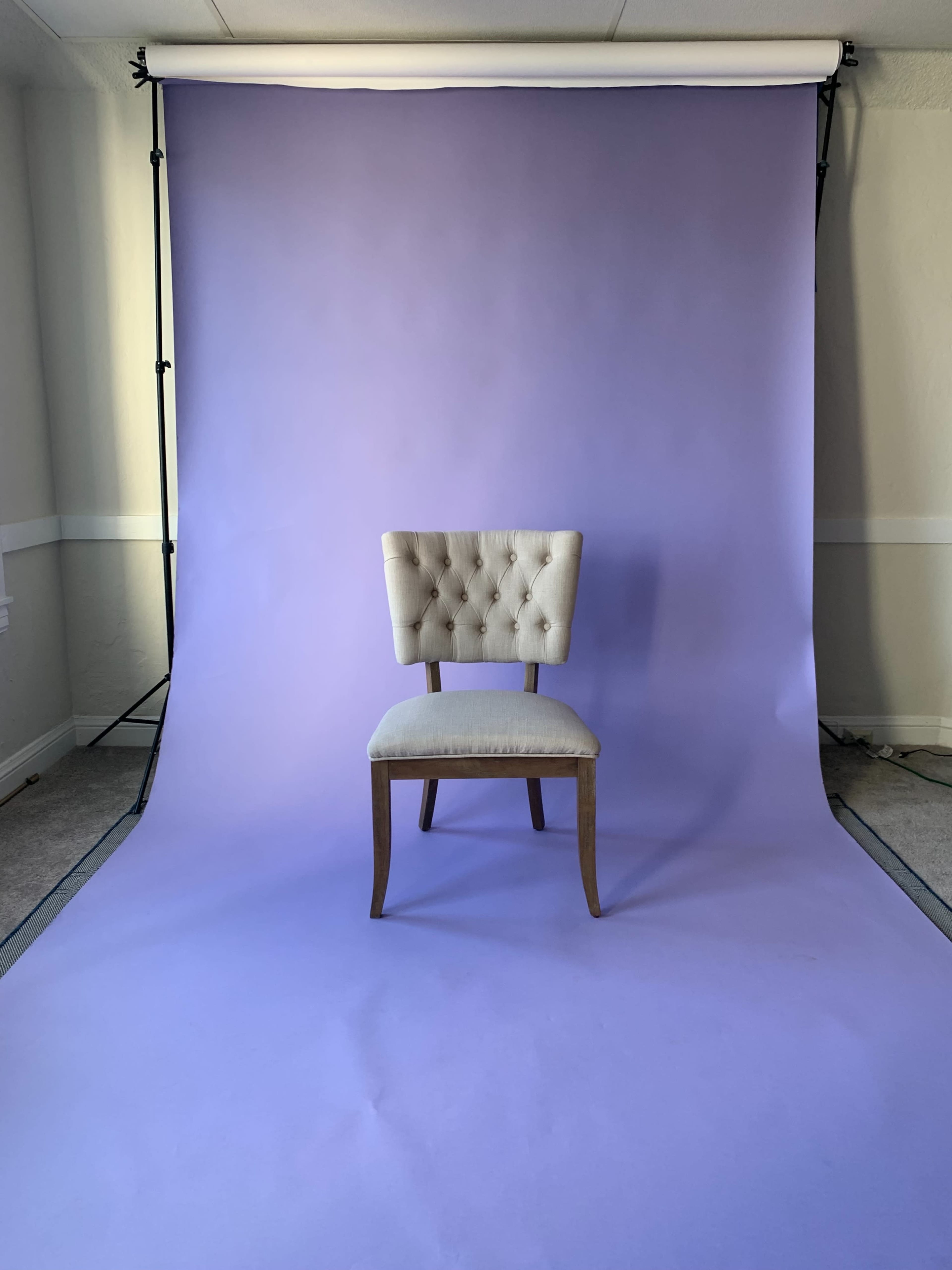 A tufted beige chair is positioned in front of a solid lavender backdrop.