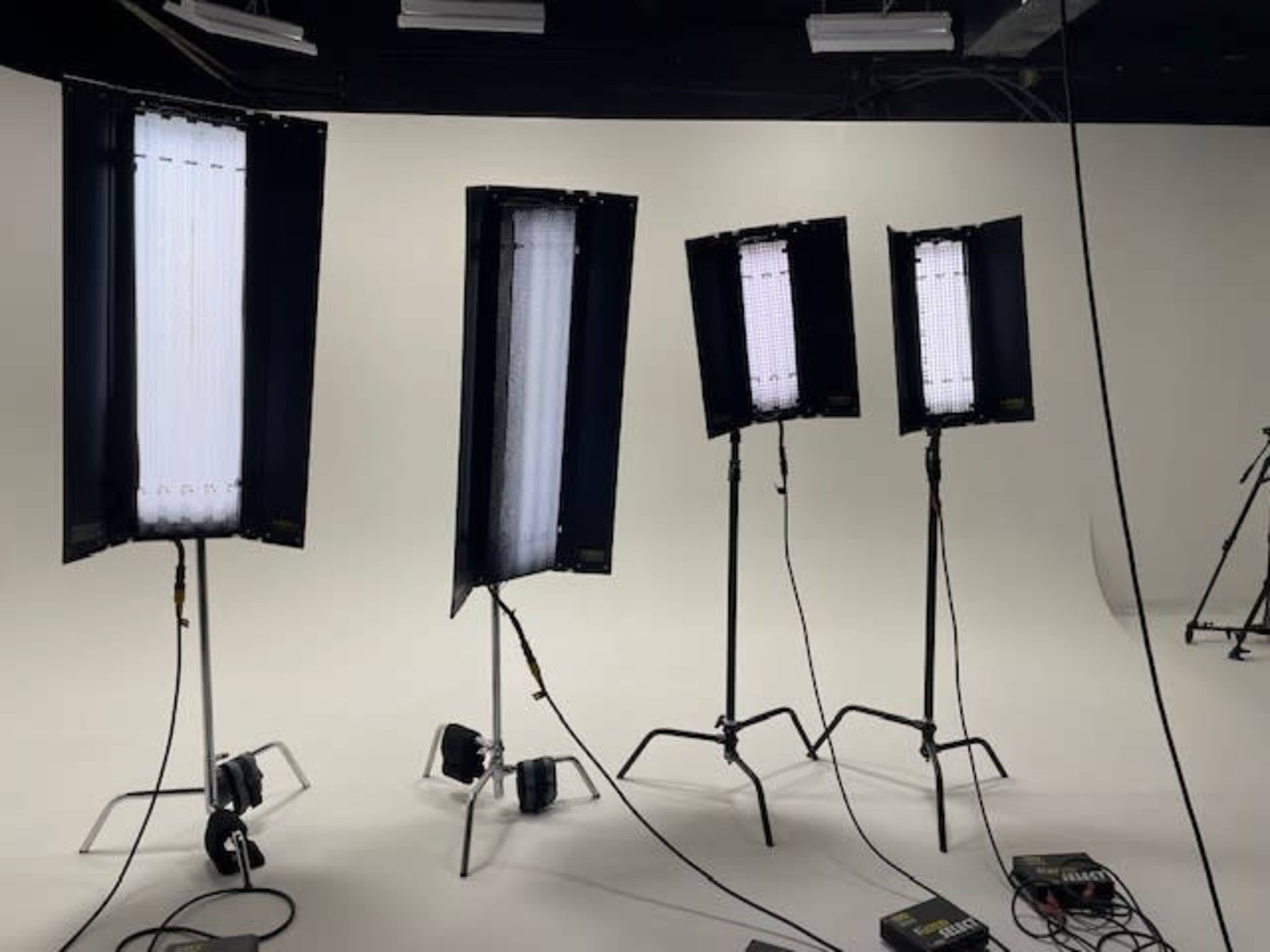 Four light stands with softbox lights set up in a studio environment against a white backdrop.