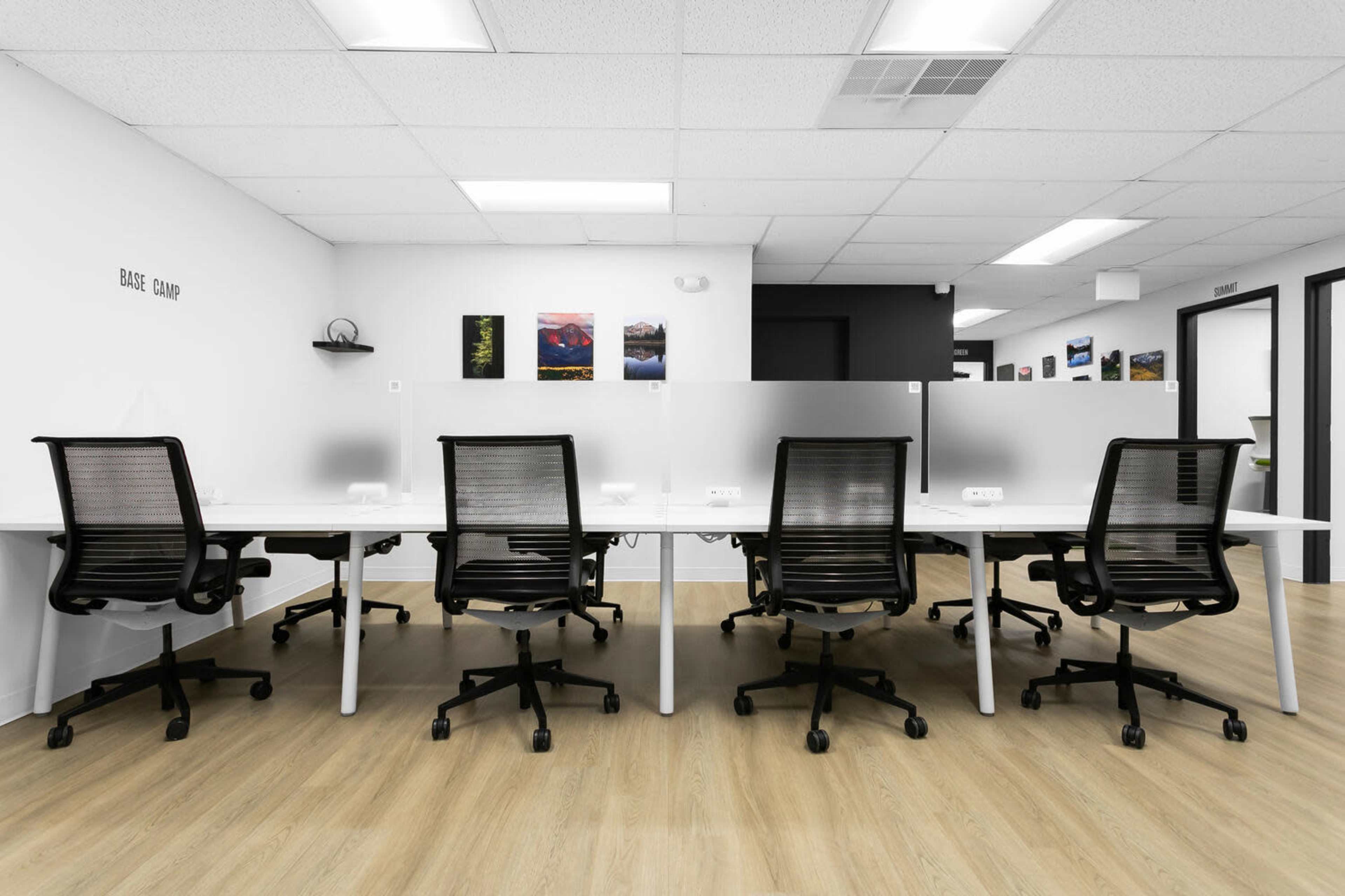 The image shows a modern office space with multiple white desks and ergonomic chairs separated by translucent partitions.