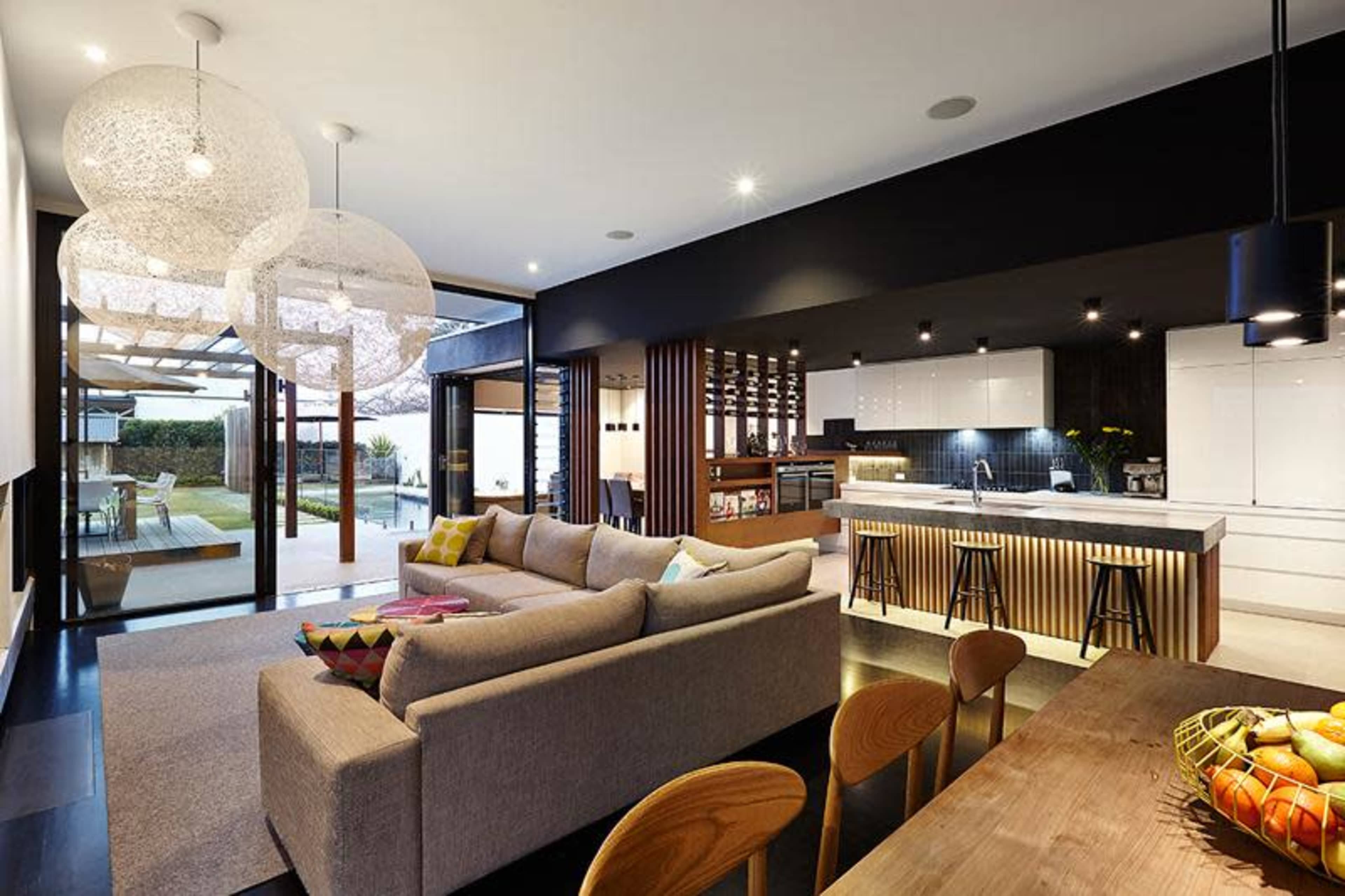 A modern open-concept kitchen and living area with a large sectional sofa, pendant lights, and a view of an outdoor patio through glass doors.