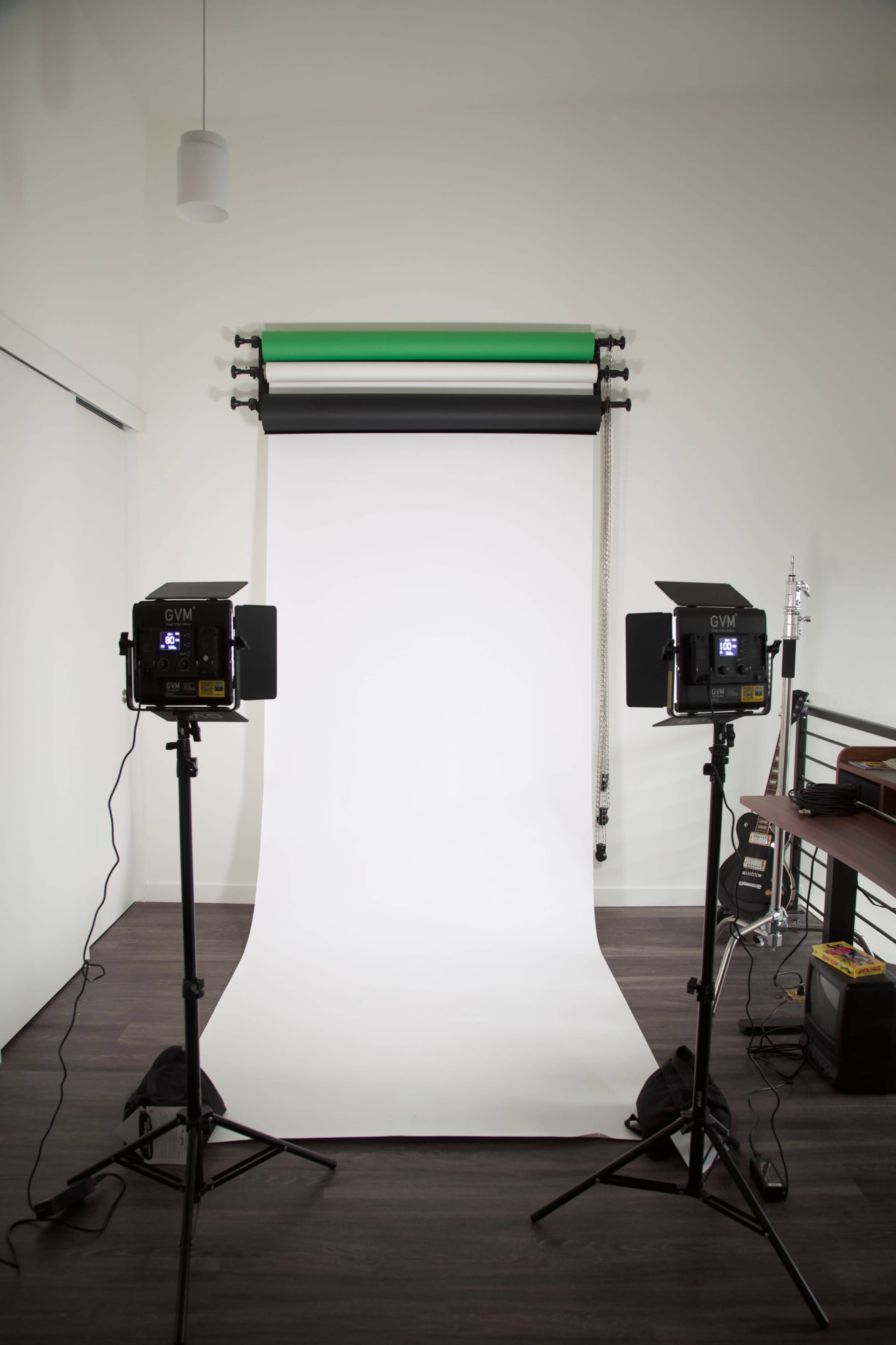A photography studio features a white backdrop with two lighting fixtures positioned on either side.