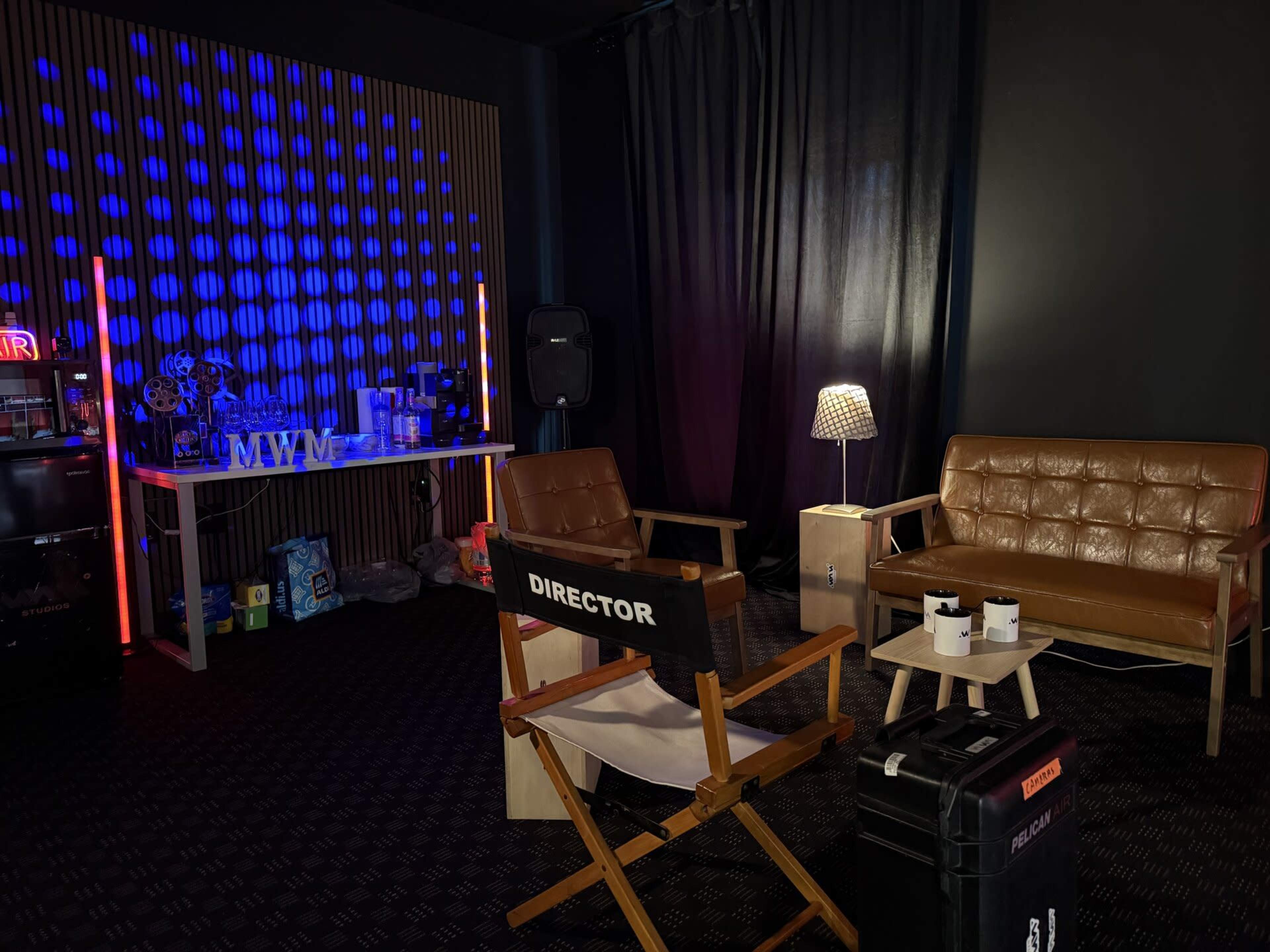 The image shows a modern studio space with a director's chair, a brown leather couch, a table with various items, and ambient lighting creating a vibrant atmosphere.