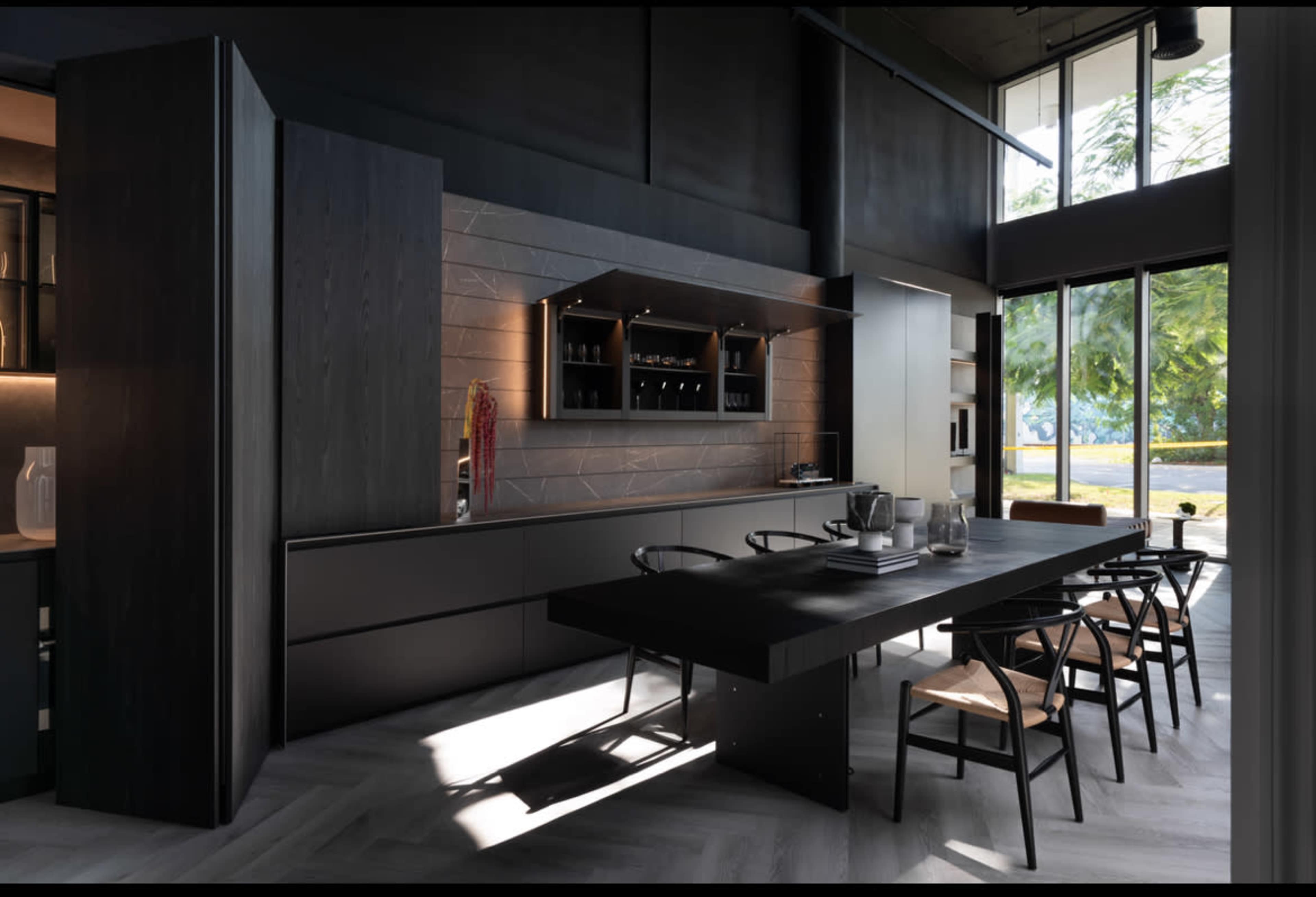 A contemporary kitchen features a dark wooden dining table and cabinetry, with large windows allowing natural light to illuminate the space.
