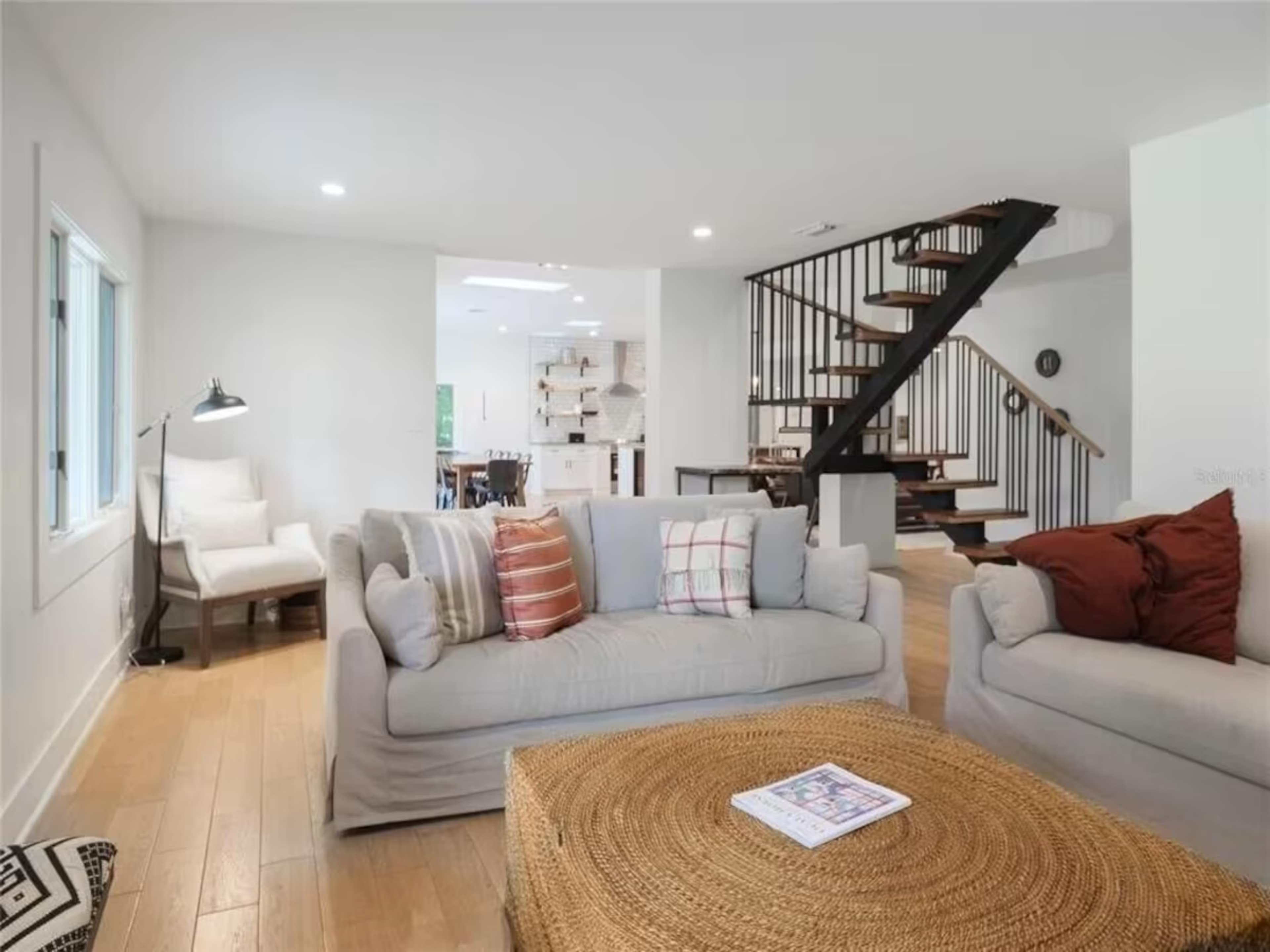 A modern living room with light-colored sofas, a large round coffee table, and a staircase leading to an upper level.