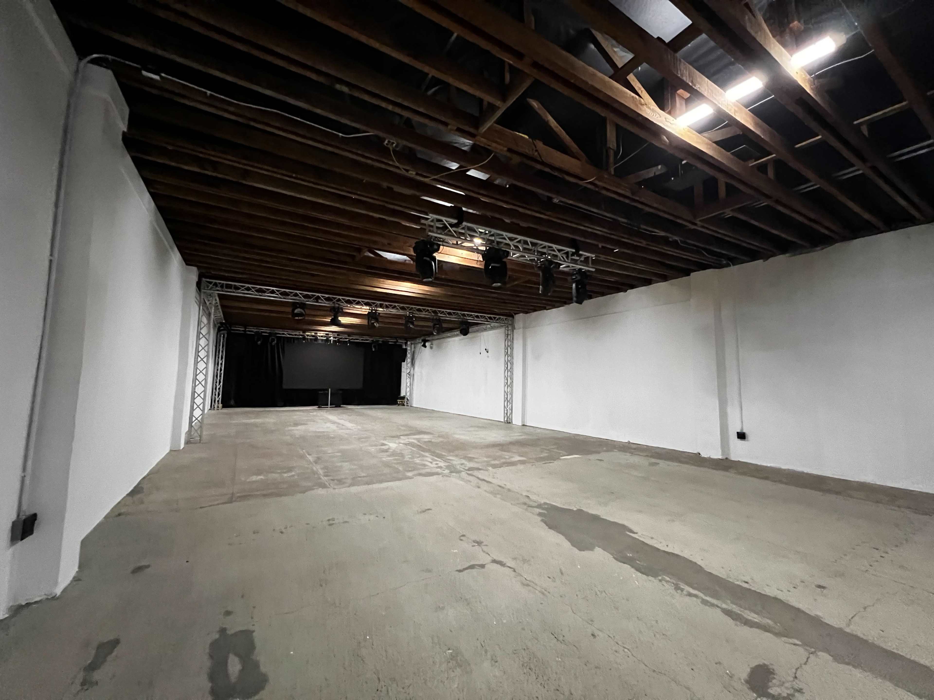A spacious, empty indoor area with exposed wooden beams, concrete flooring, and black curtains at one end.