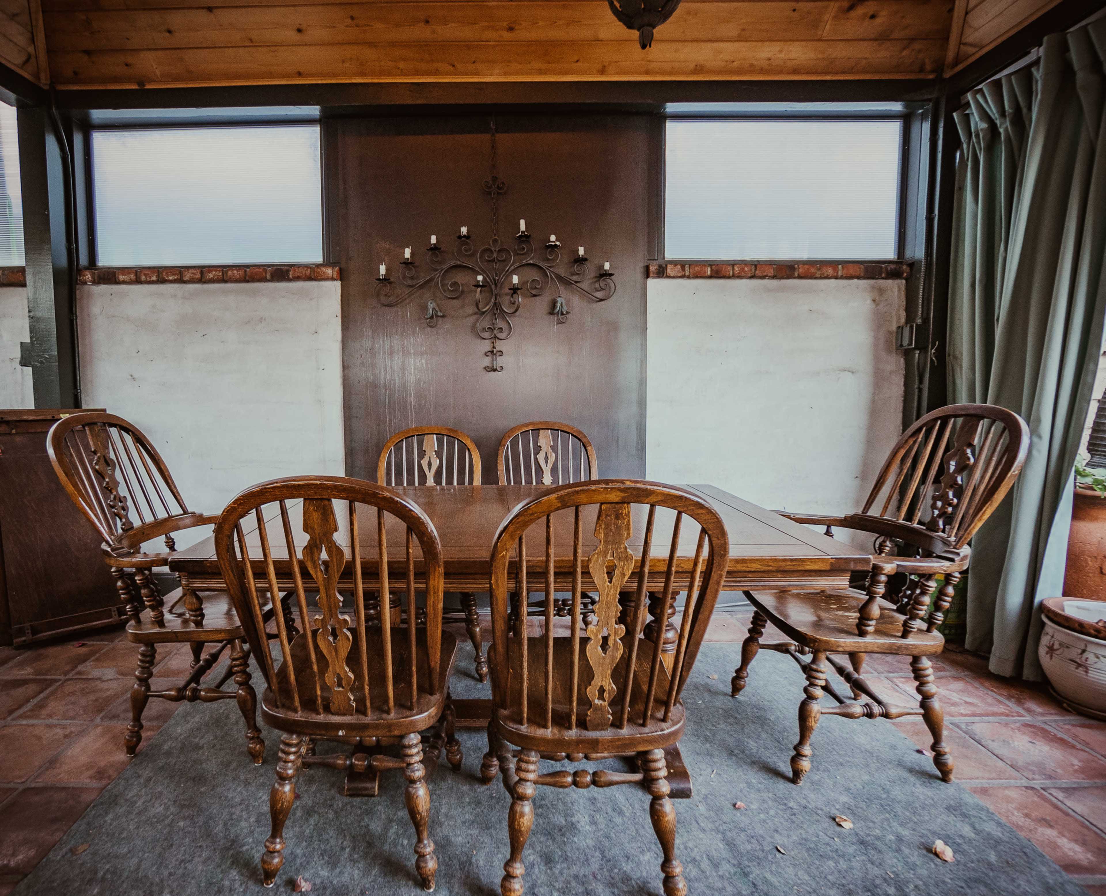 A wooden dining table surrounded by six matching chairs sits in a room with a chandelier and a decorative wall behind it.