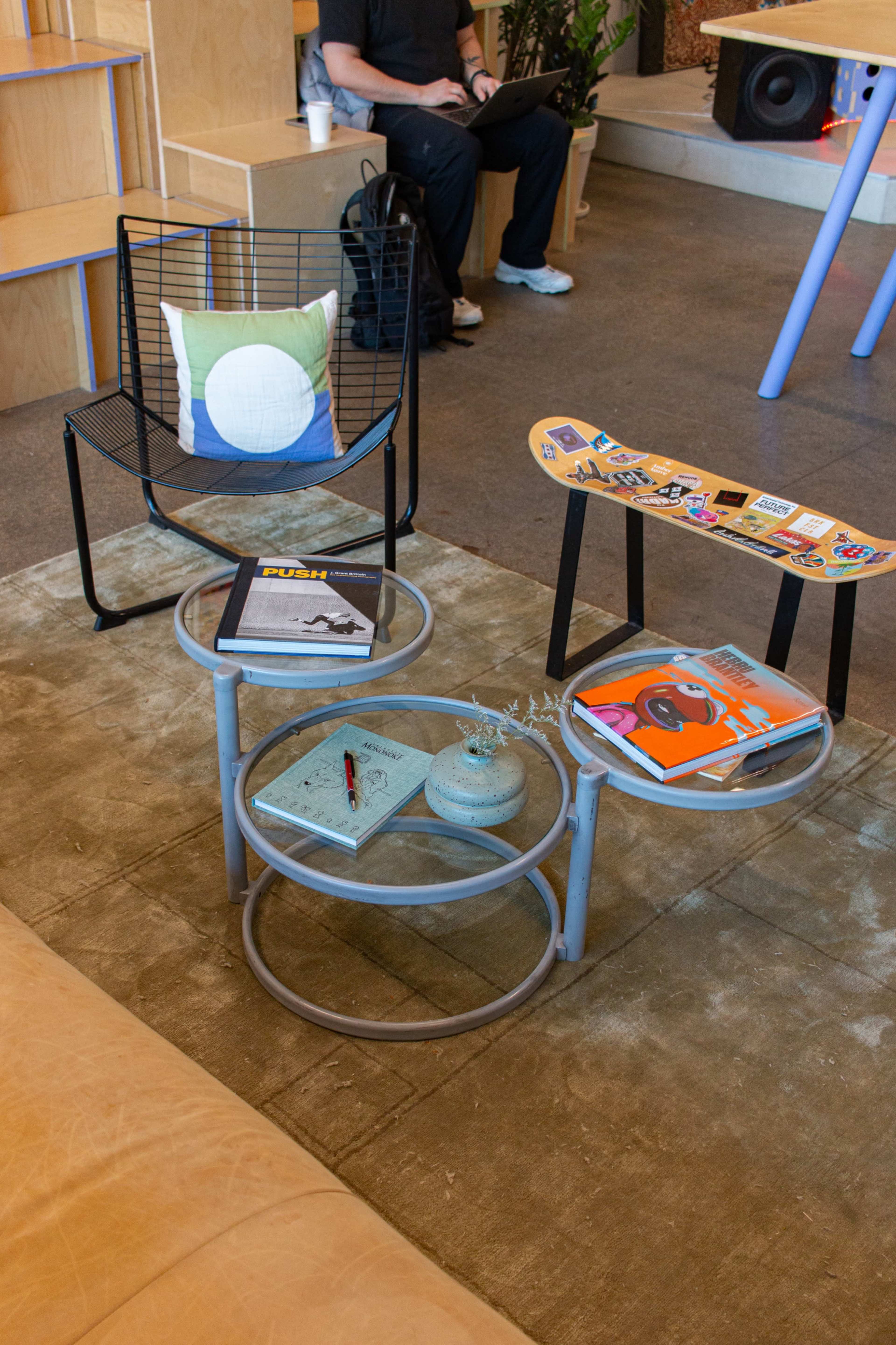 A modern living area features a circular coffee table with magazines and a decorative plant, accompanied by a unique chair and a colorful bench.