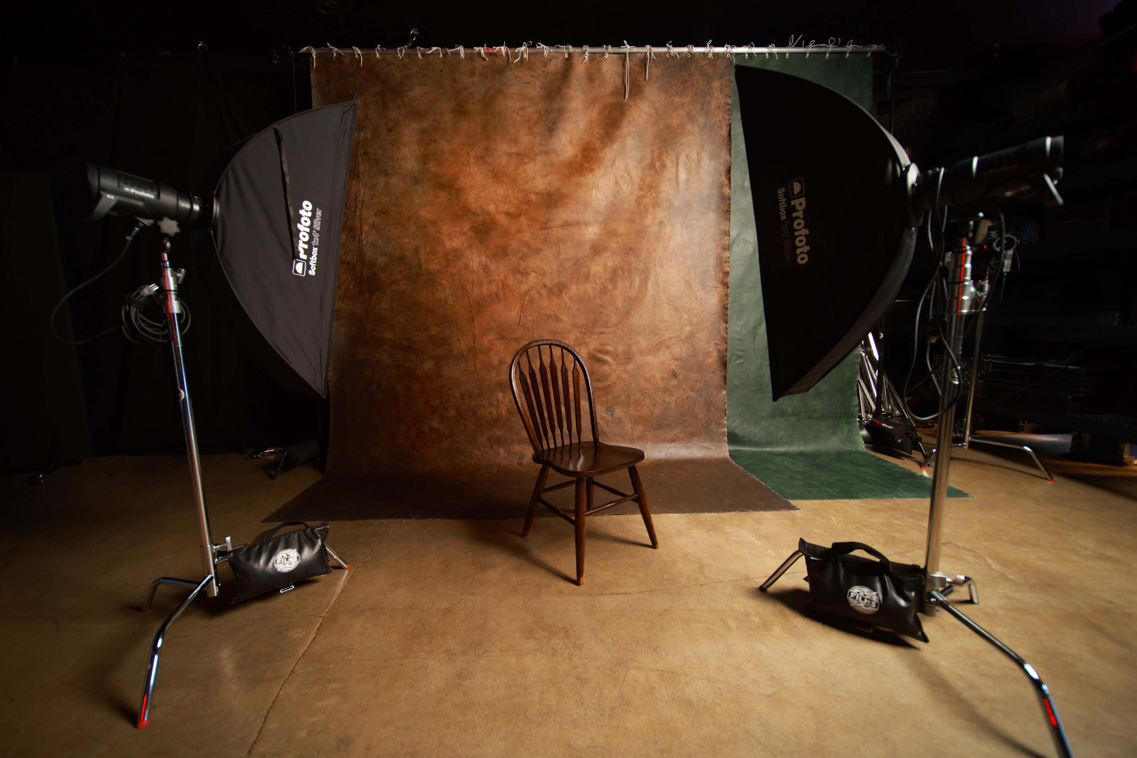 The image features a photography studio setup with a wooden chair positioned in front of a textured backdrop, flanked by two softbox lights.