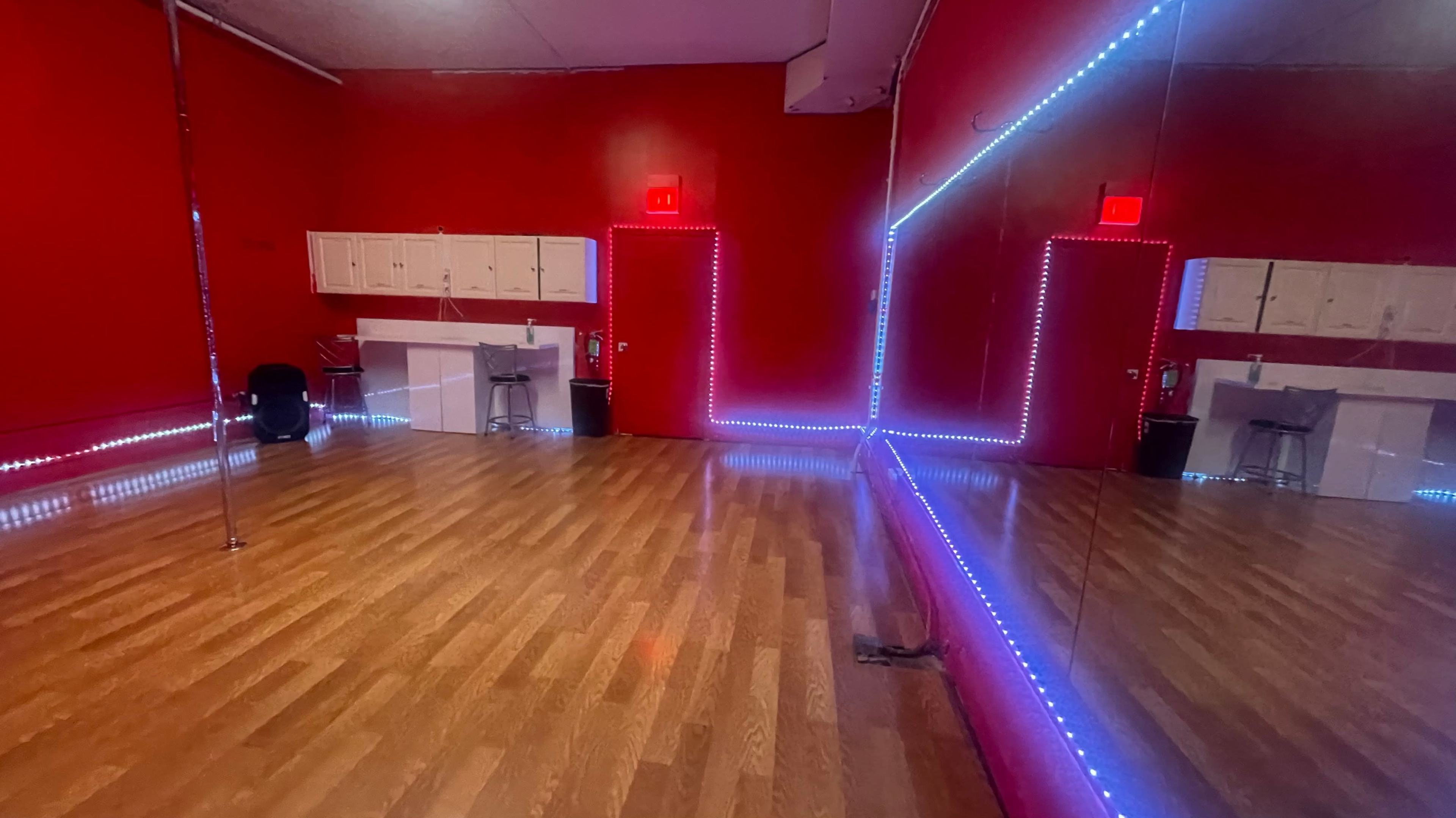 A dance studio with red walls, wooden flooring, and mirrored walls illuminated by LED lights.