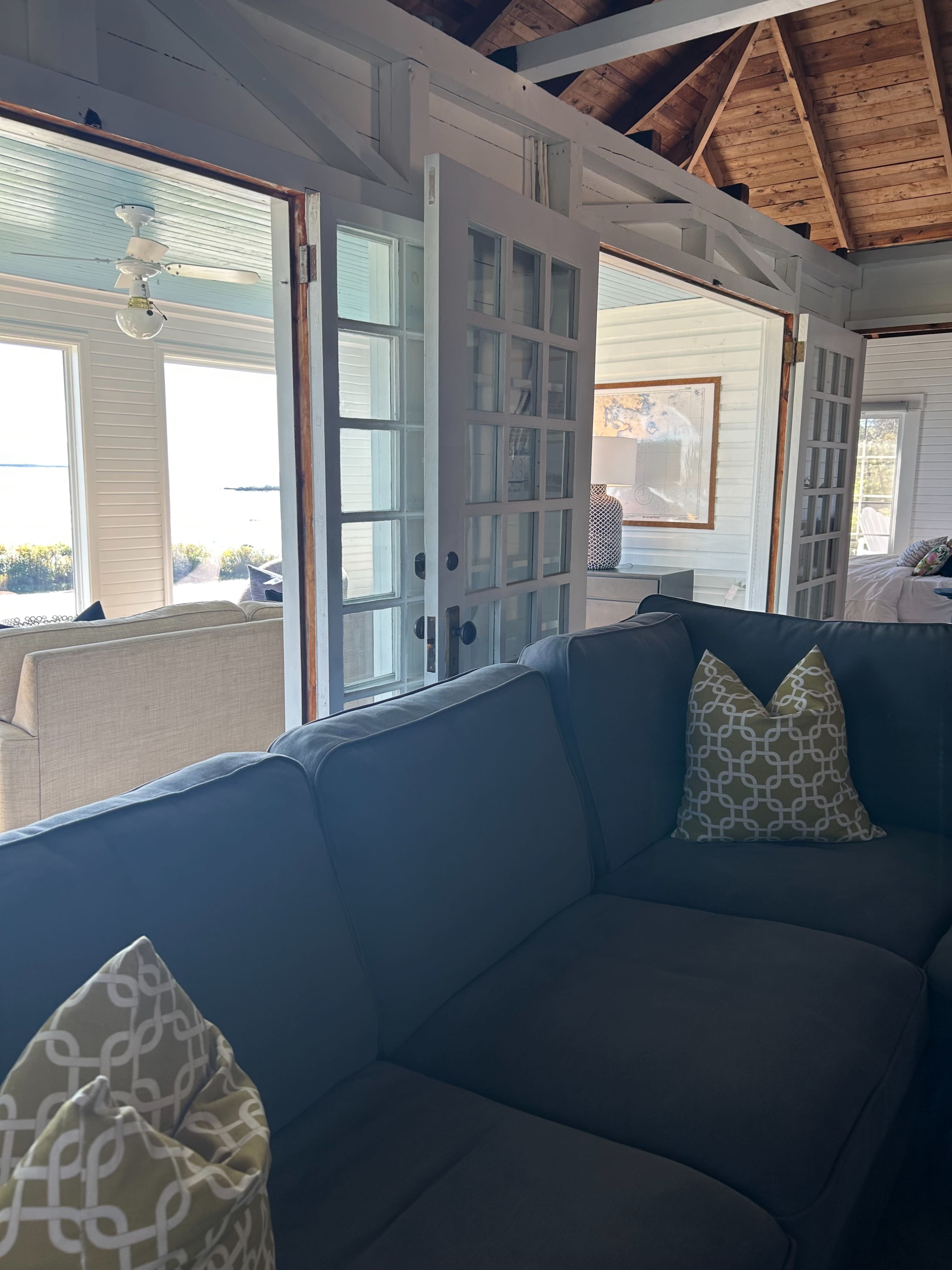 The image shows a cozy living space with a gray sofa adorned with patterned pillows, and glass doors leading to an outdoor view.
