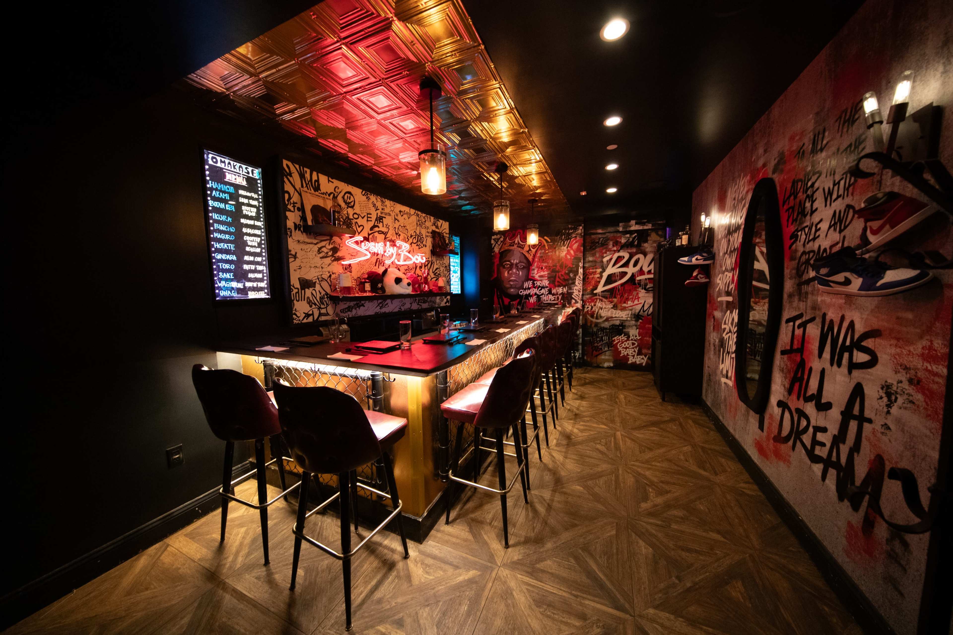 The image shows an interior of a bar with graffiti-covered walls, a decorative ceiling, and illuminated seating along a sleek bar counter.
