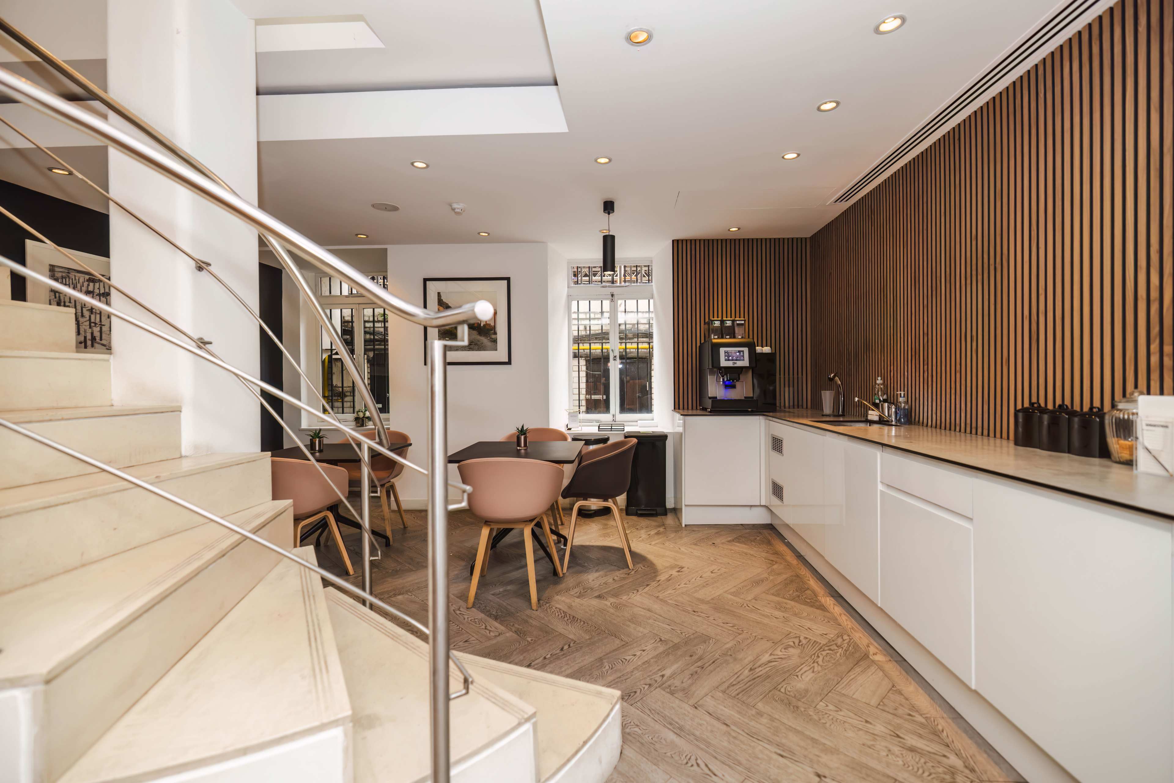 A modern interior features a staircase leading to a seating area with chairs and a counter, accented by wooden paneling and bright lighting.