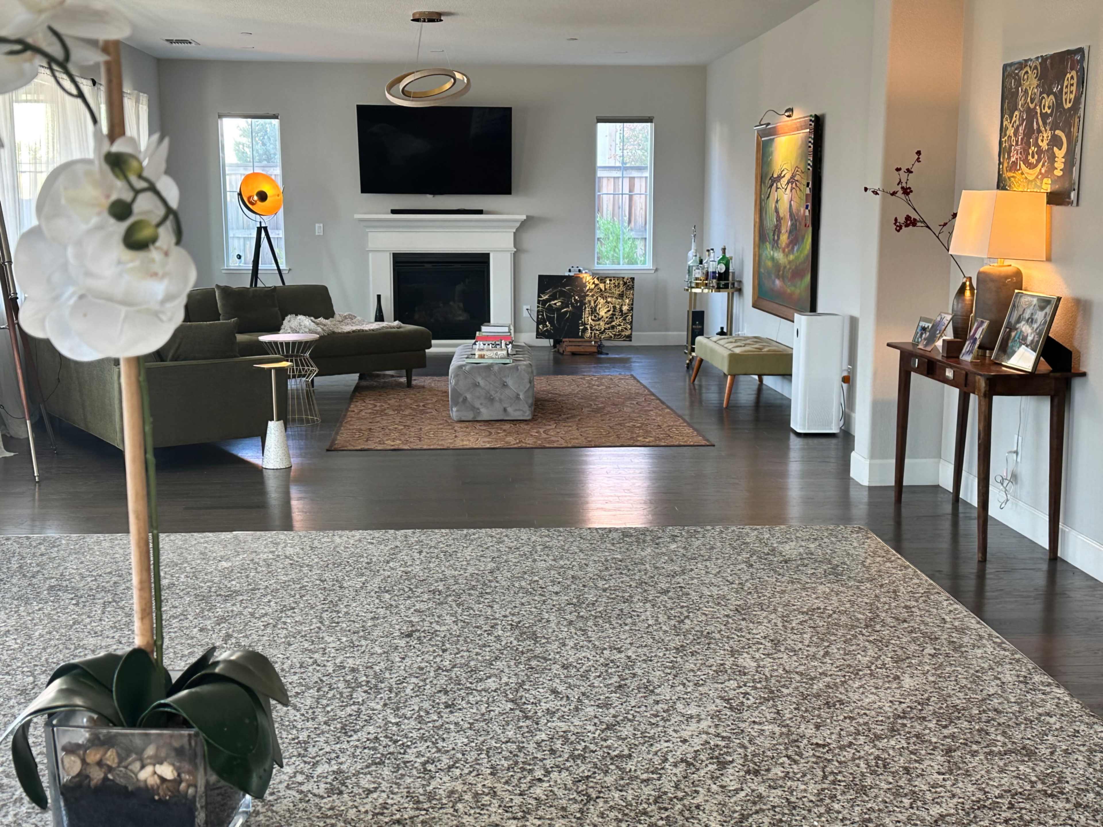 A modern living room features a green sectional sofa, a central coffee table, a large TV mounted on the wall, and decorative artwork throughout.