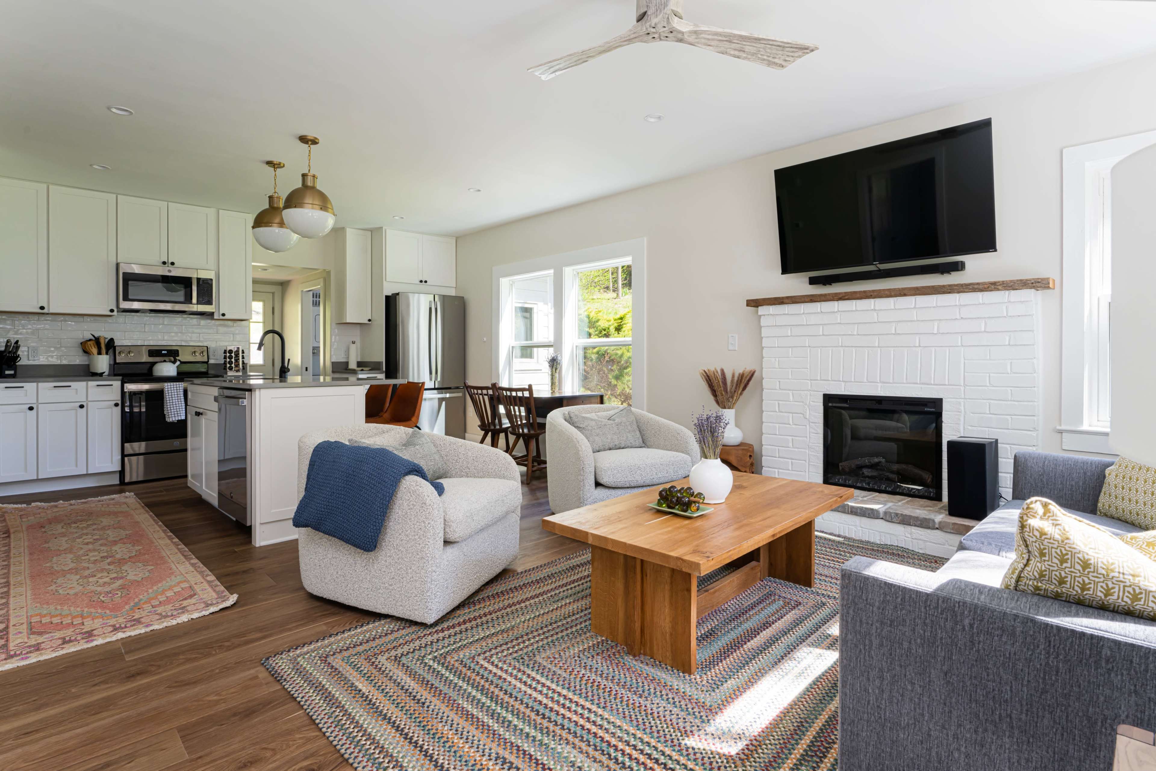 A modern living room features a fireplace, a coffee table, and comfortable seating, with an adjacent kitchen visible in the background.