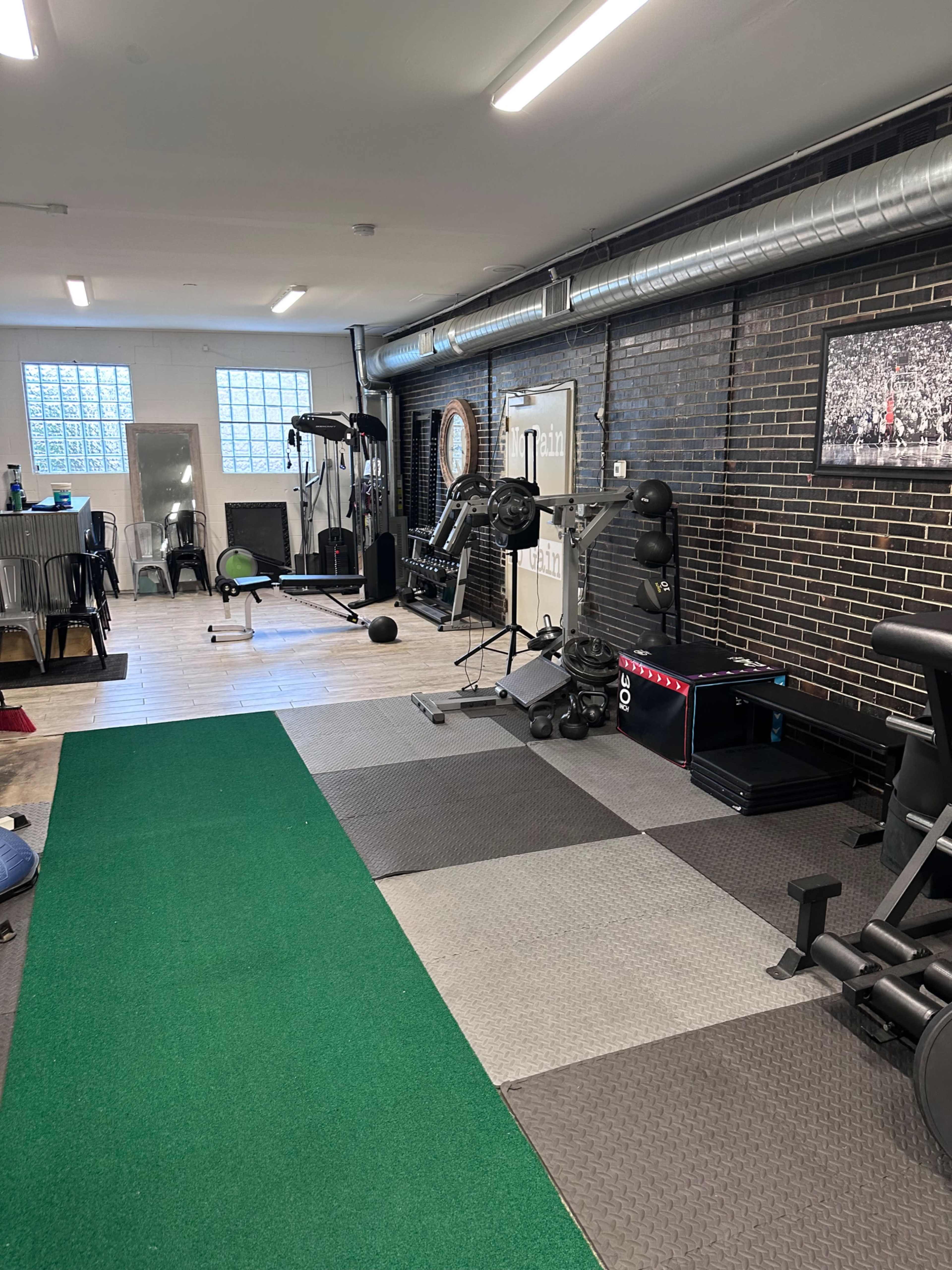 A gym interior featuring exercise equipment, including weights, a squat rack, and a green exercise mat on the floor.