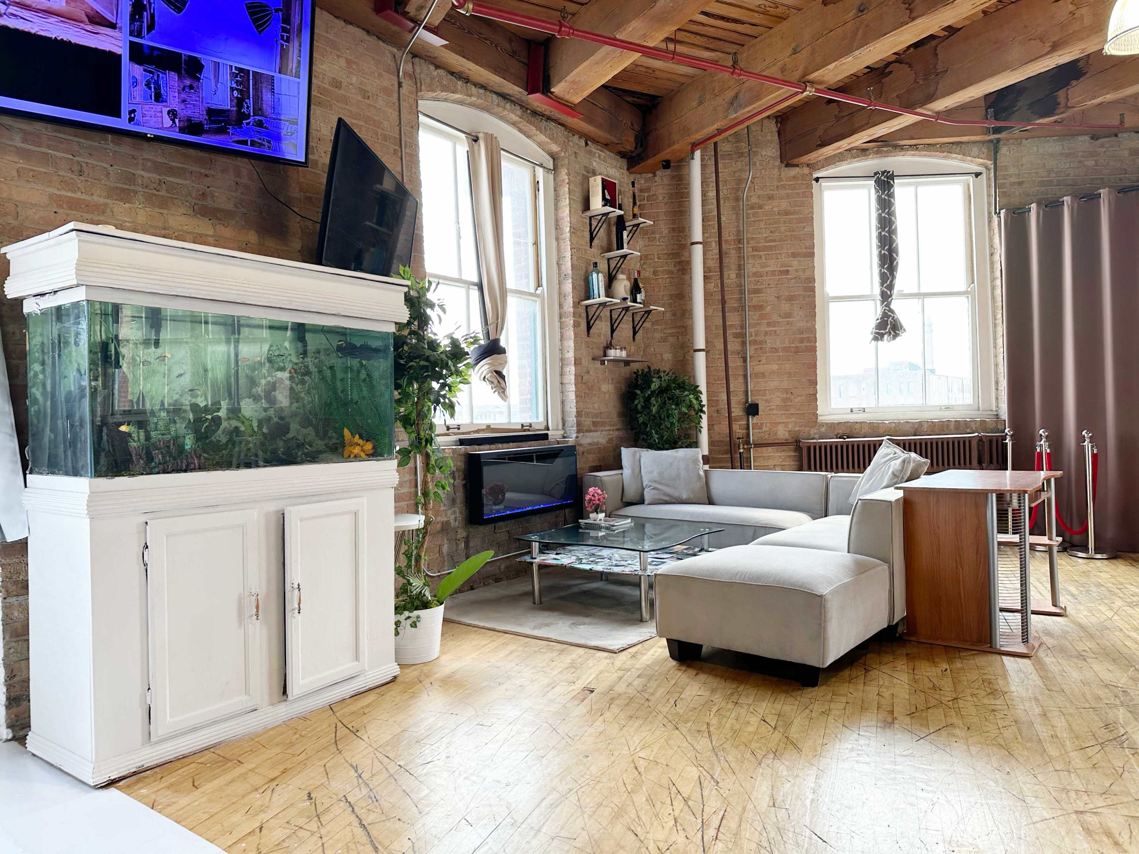 A modern living area with a large aquarium, a sectional sofa, a glass coffee table, and wooden beams on the ceiling.