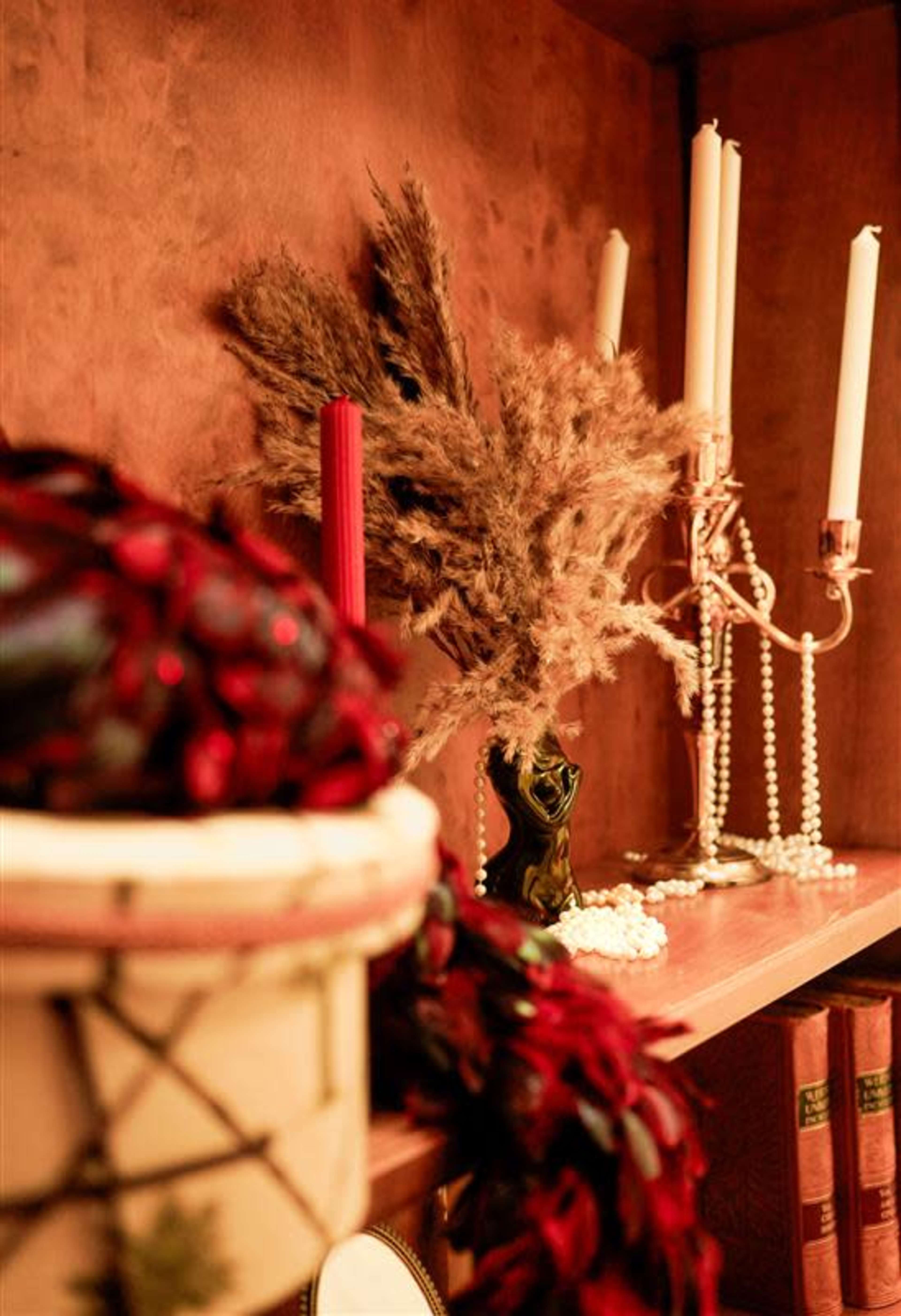 The image features a shelf displaying decorative items, including candles, a dried bouquet, and books.