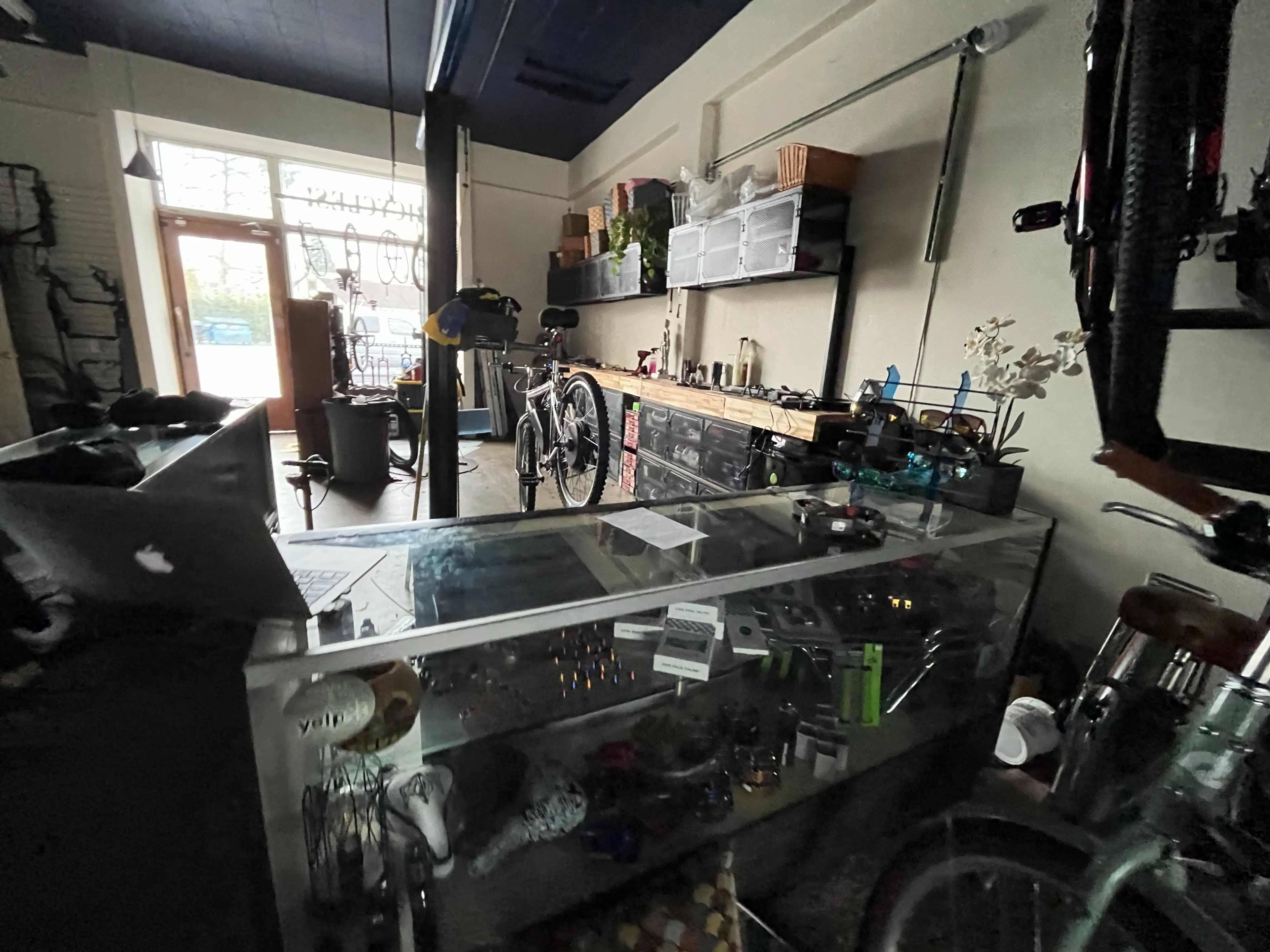 The image shows the interior of a bicycle shop with a counter display, bicycles, and various tools and accessories on shelves.