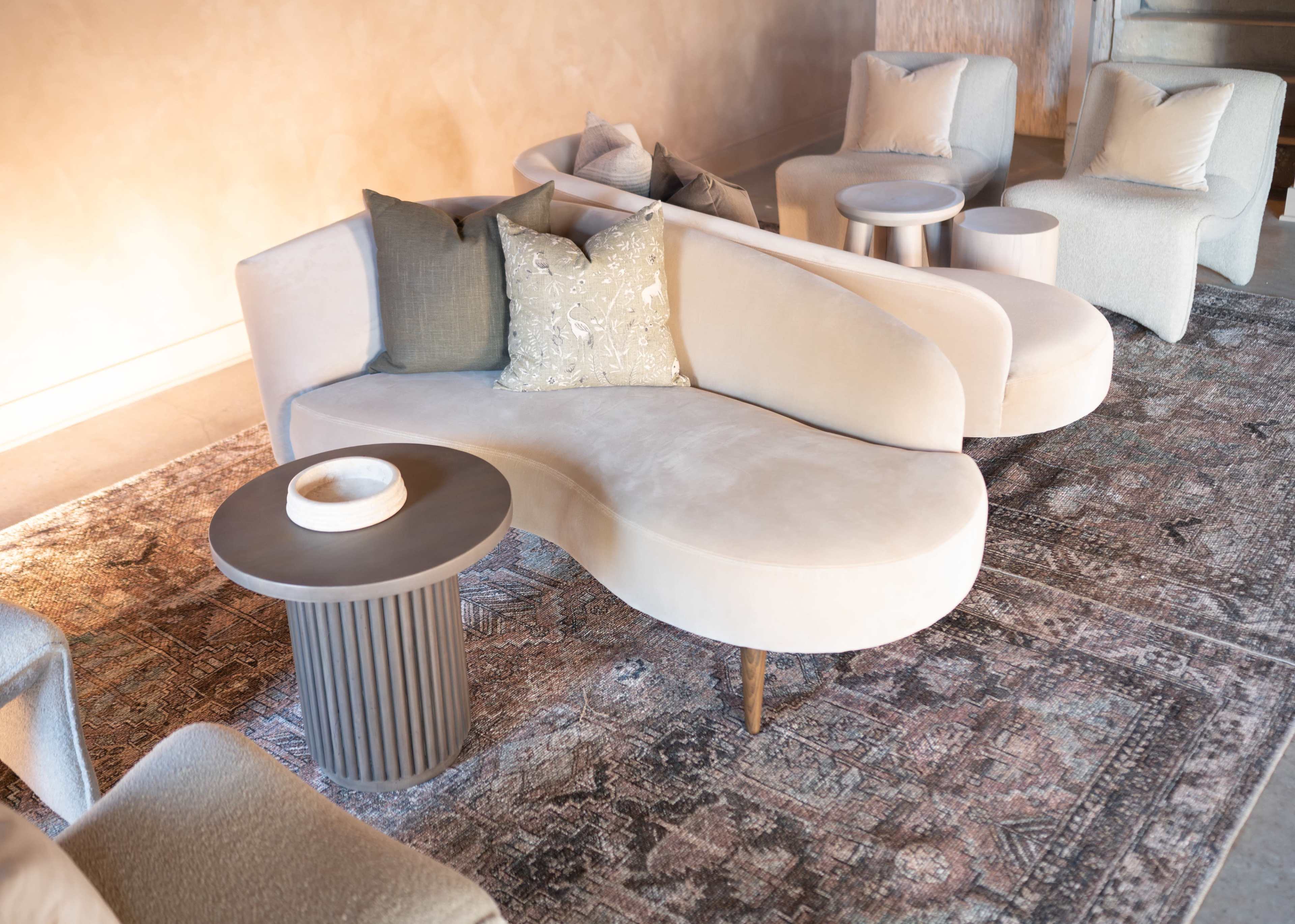 A modern living space with a curved light-colored sofa, accent pillows, and round side tables arranged on a patterned area rug.