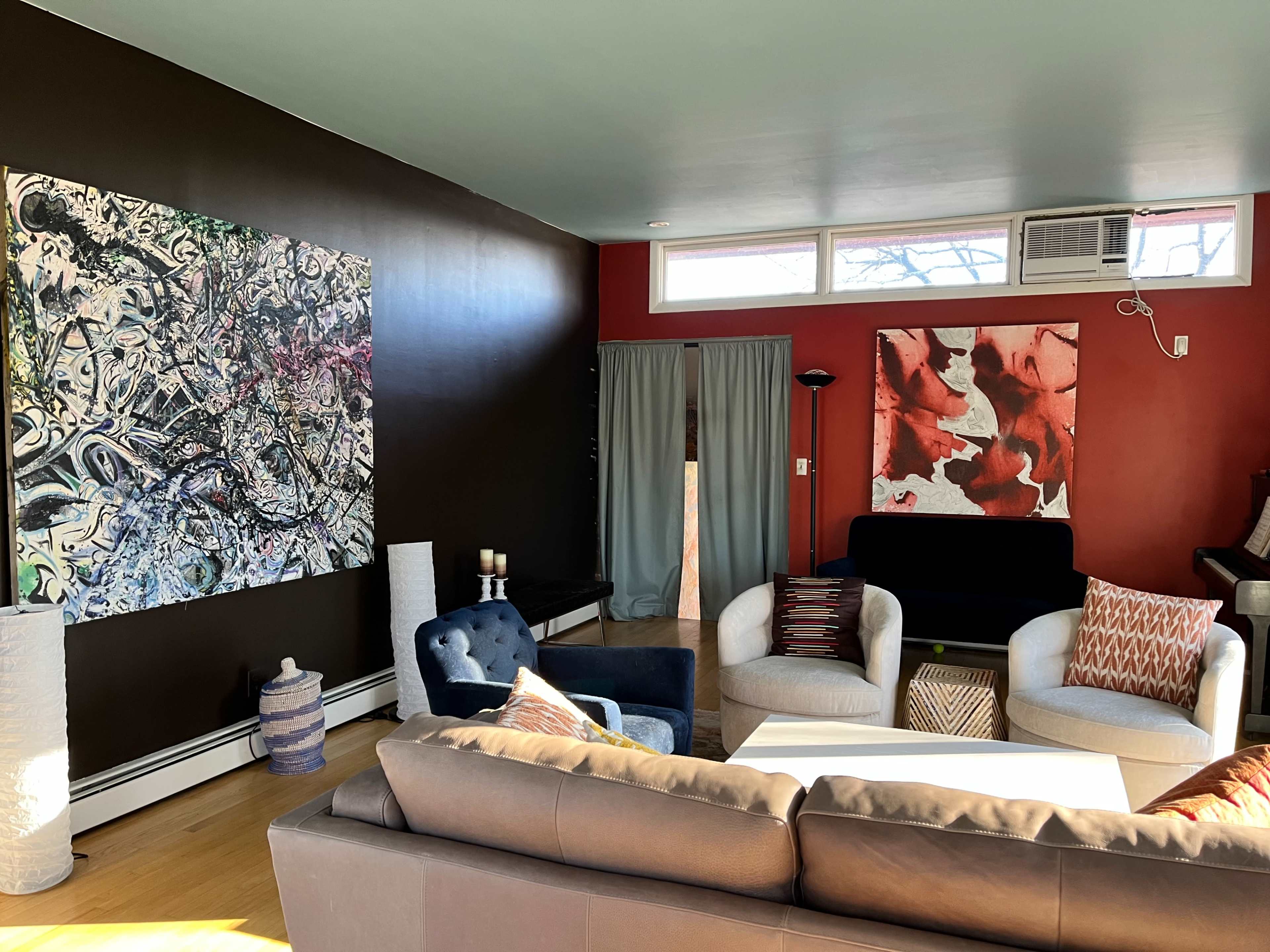 A modern living room featuring a mix of colorful wall art, a sectional sofa, and two accent chairs.