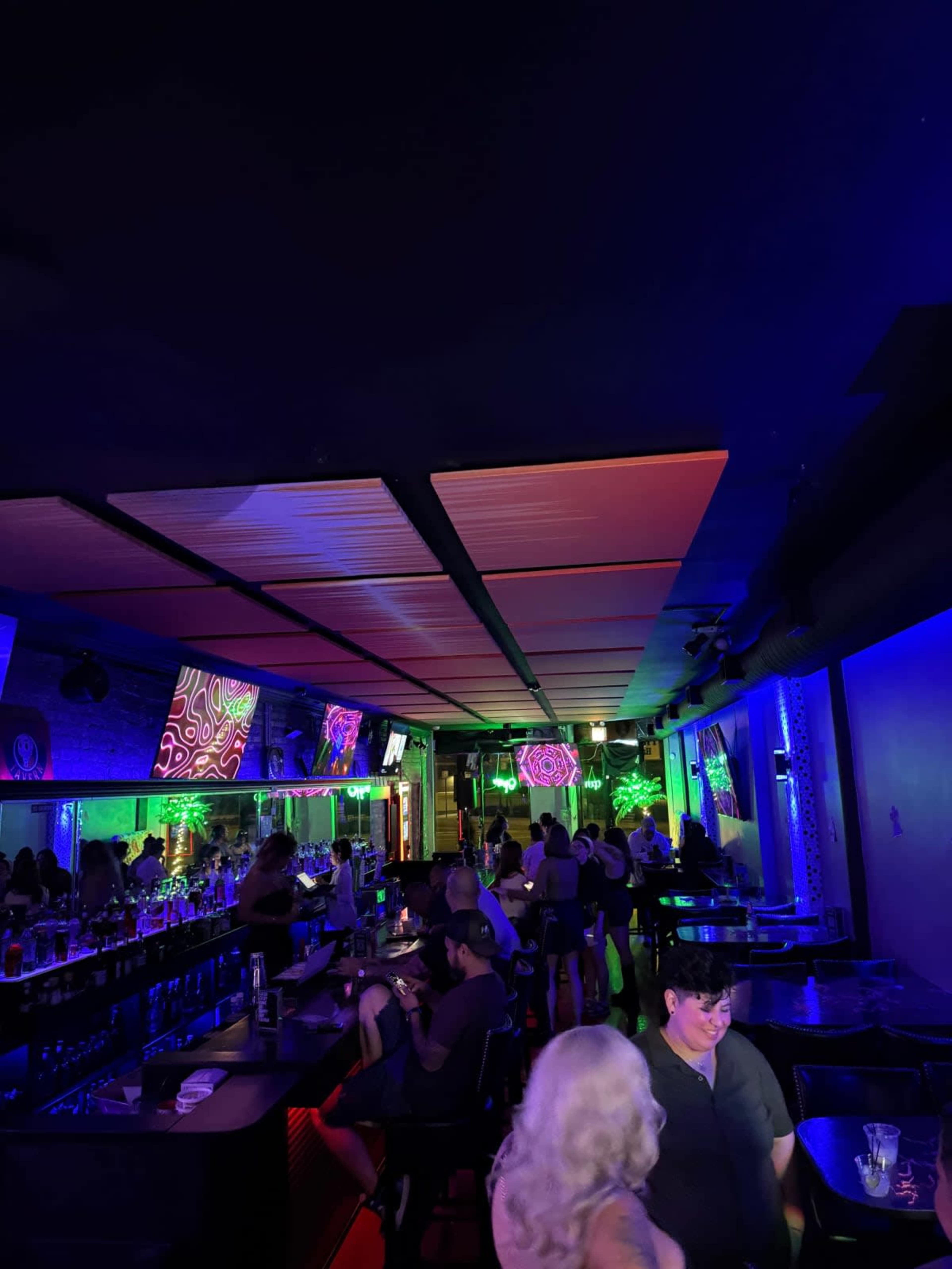 The image shows a vibrant bar scene with colorful lights and several patrons enjoying the atmosphere.