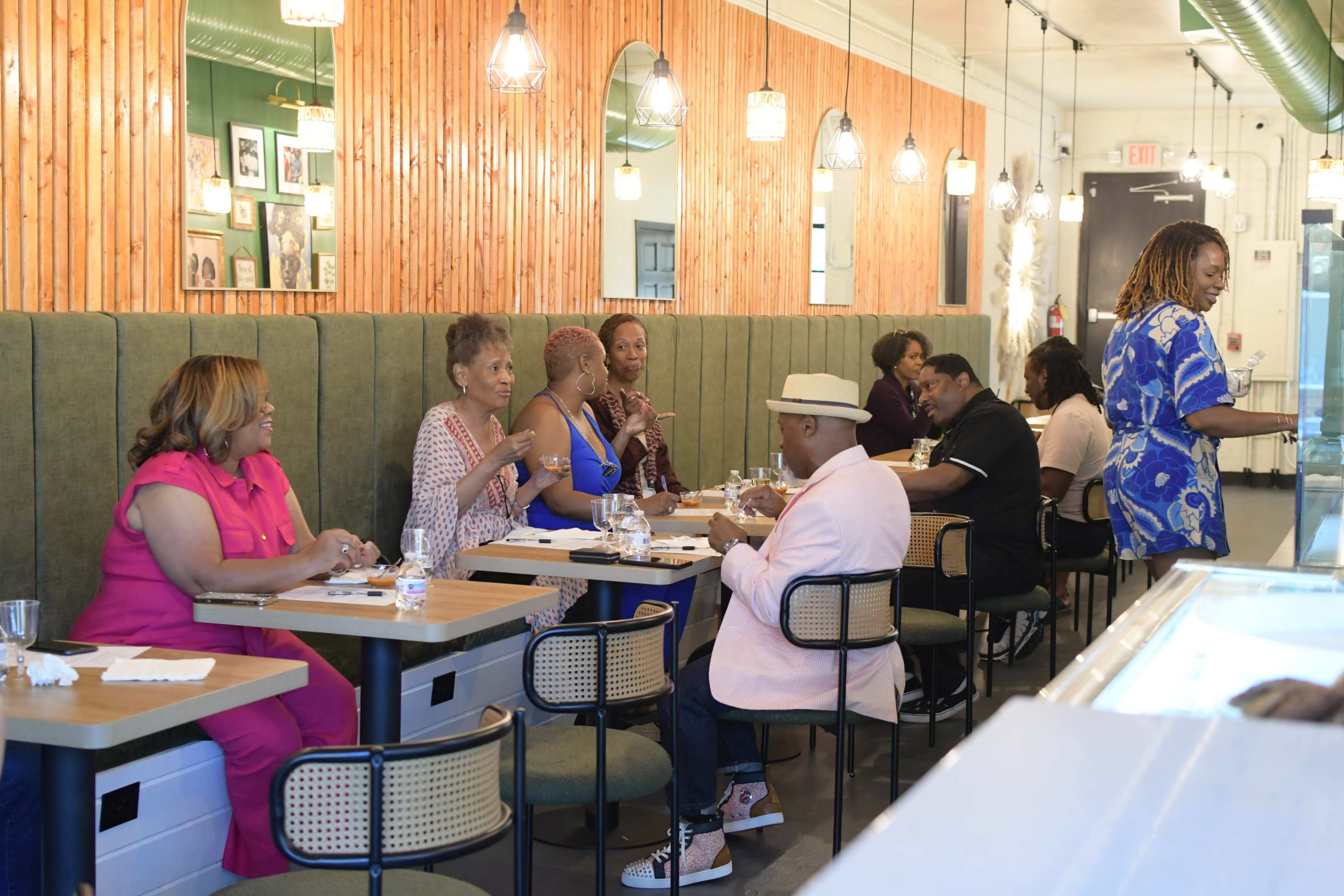 A group of people is dining at tables in a restaurant with wooden walls and bright lighting.