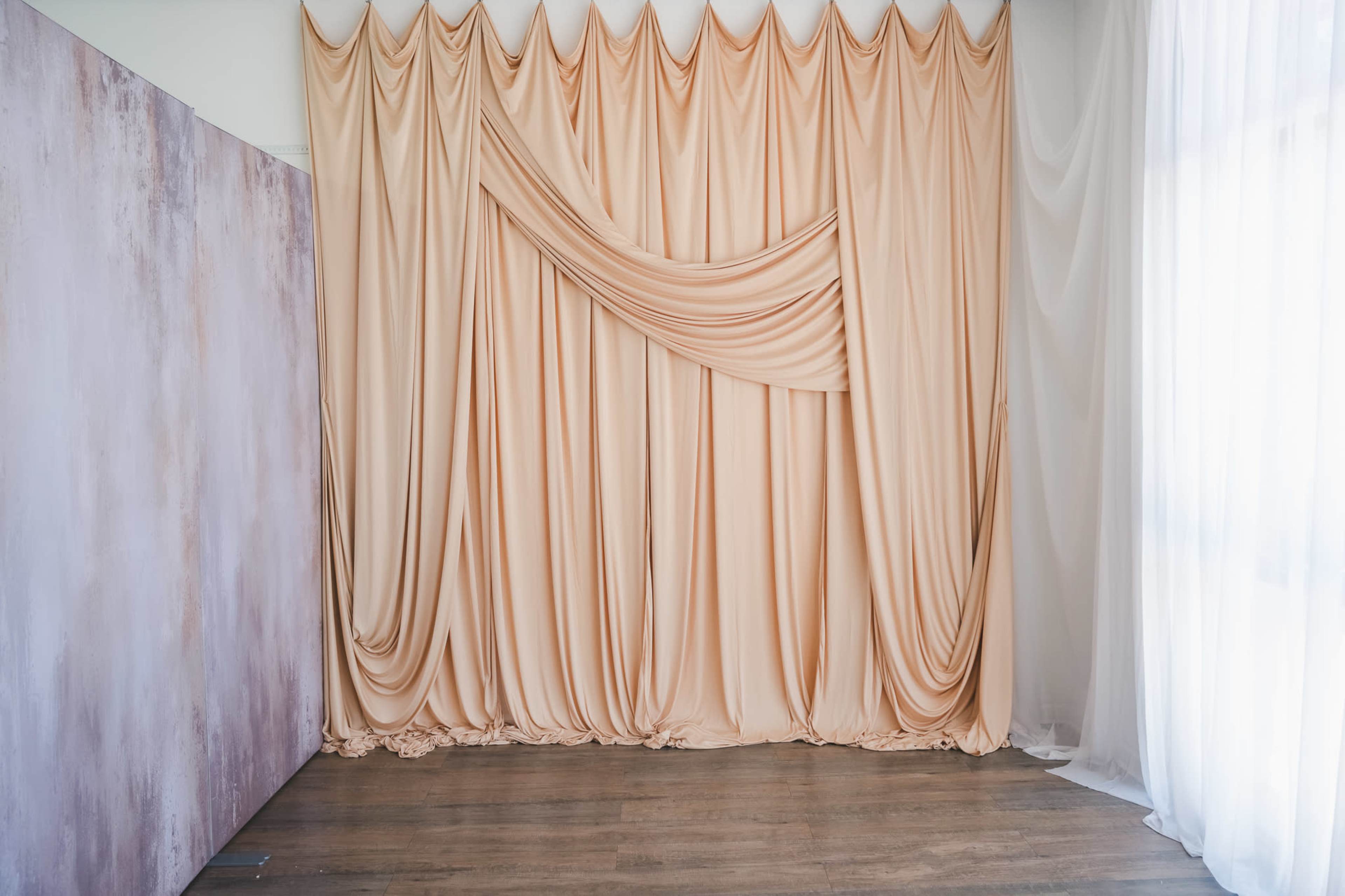 The image features a fabric backdrop with draped beige curtains and a textured purple wall on the left.