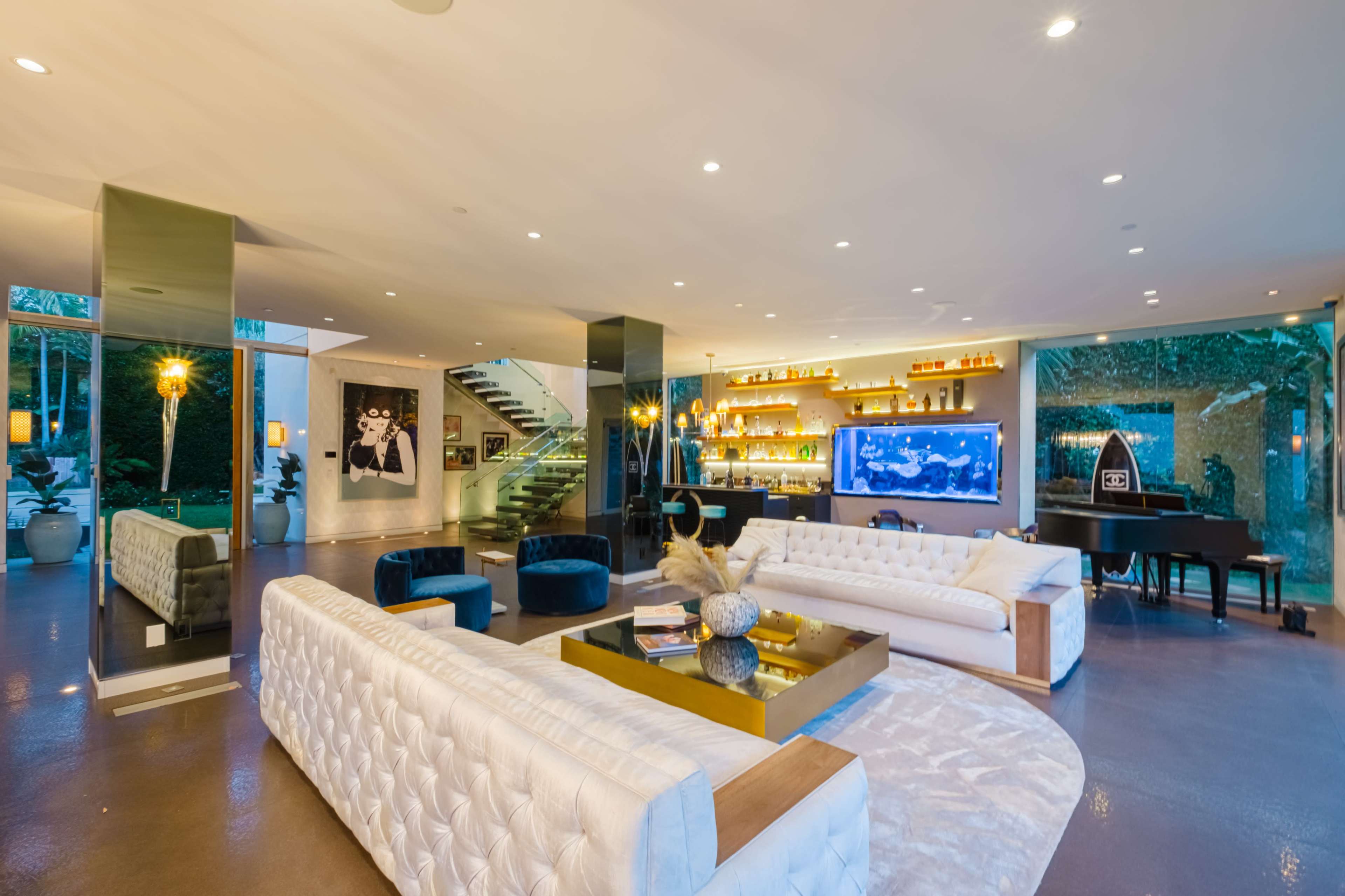 A modern living room with white sofas, a large television, a staircase, and decorative lighting.