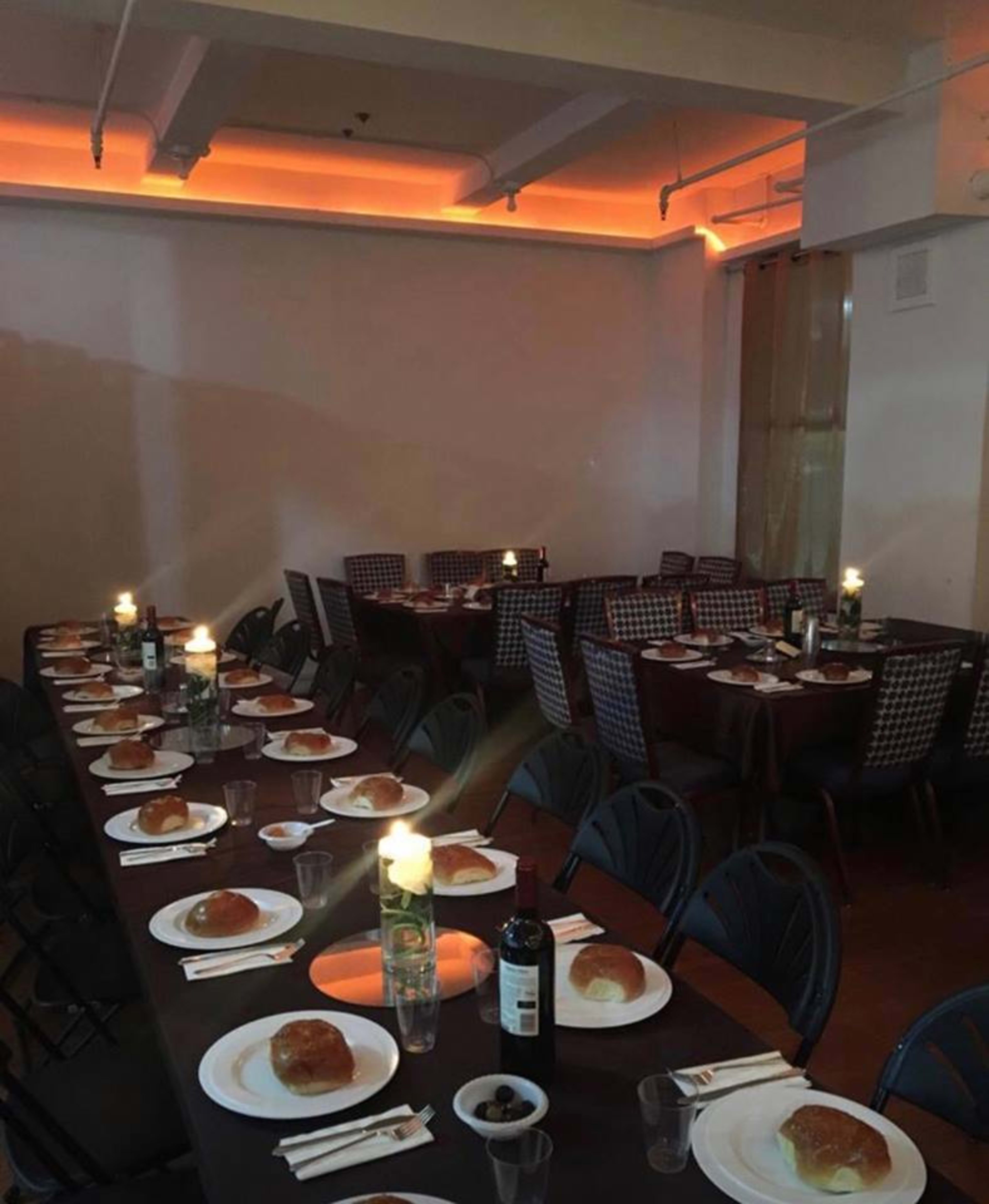 A long banquet table is set with plates of bread rolls and glassware in a dimly lit room.