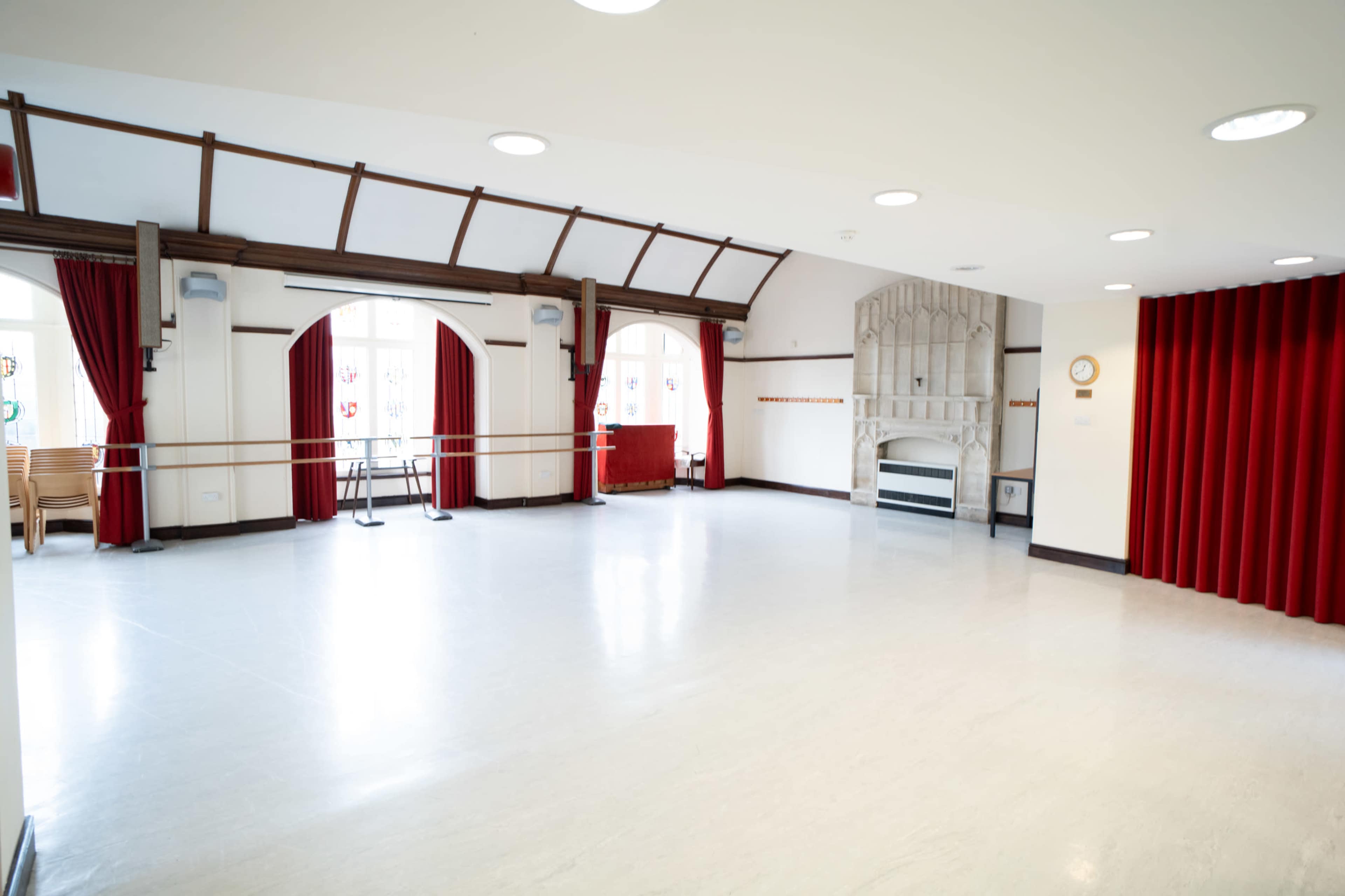 The image shows a spacious, well-lit room with white flooring, red curtains, and a large, ornate feature wall.