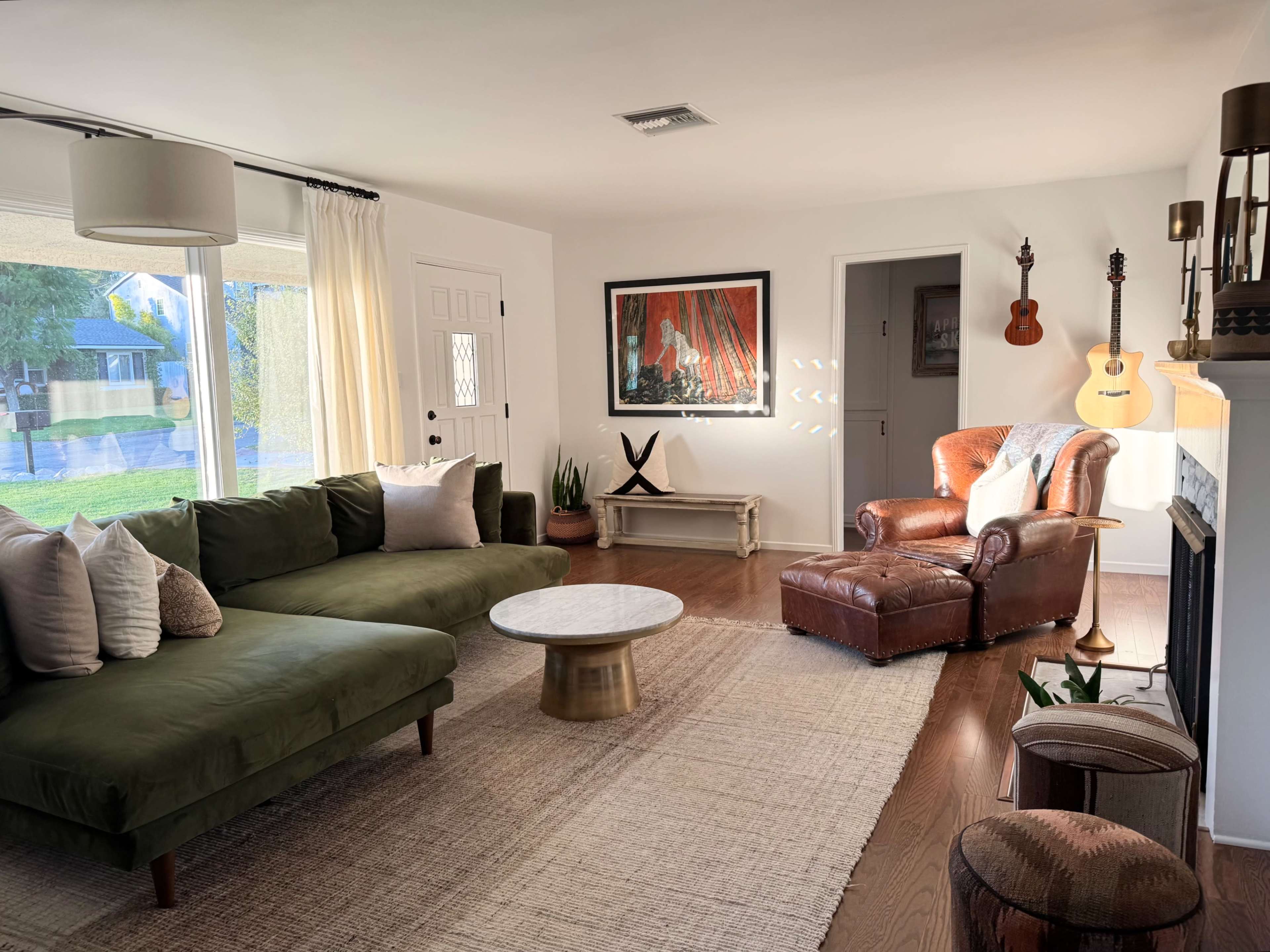 A modern living room features a green sectional sofa, a round coffee table, an armchair, and a guitar hanging on the wall.