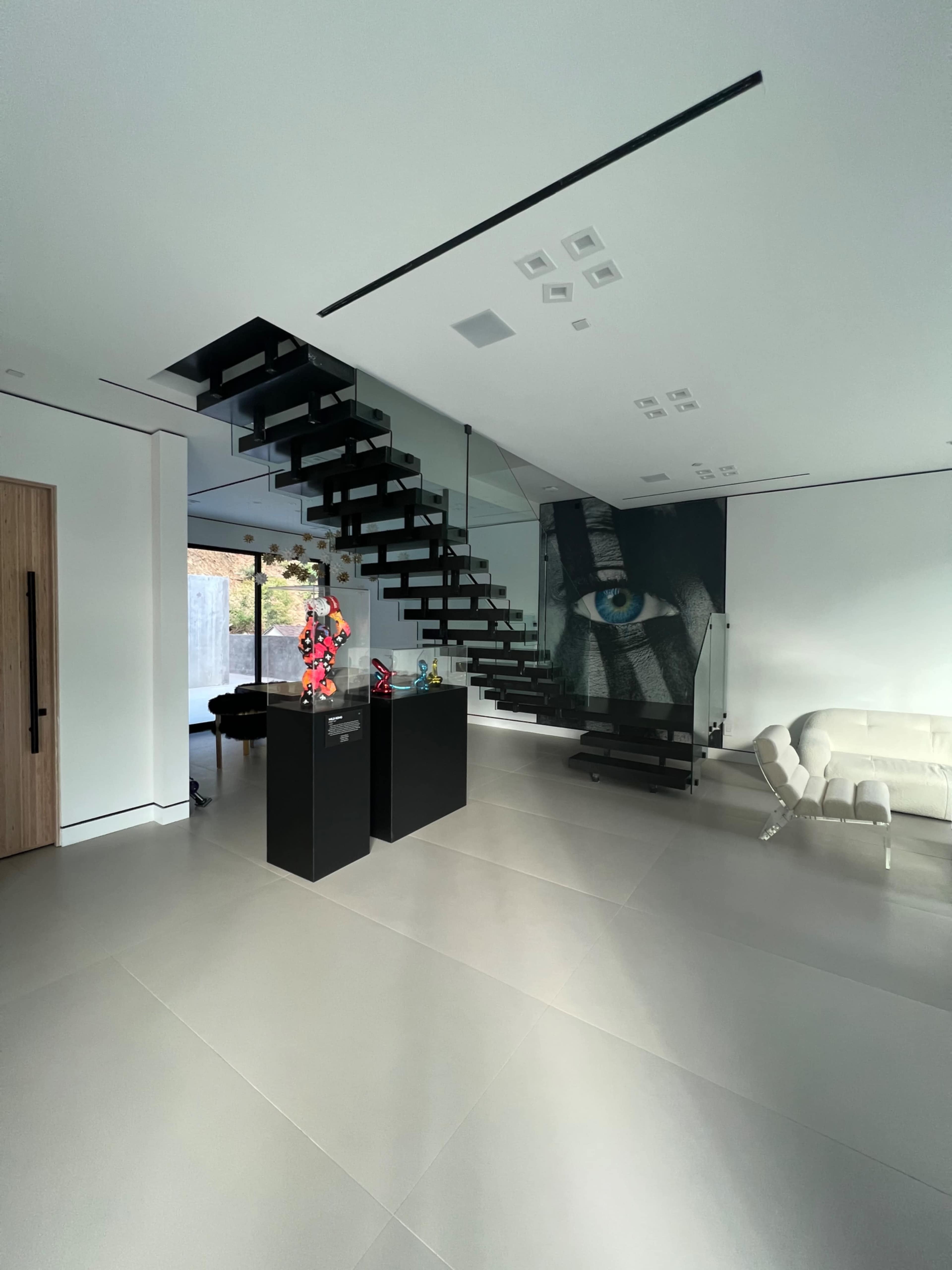 The interior features a modern staircase, a minimalist black and white aesthetic, and a large mural of an eye on the wall.